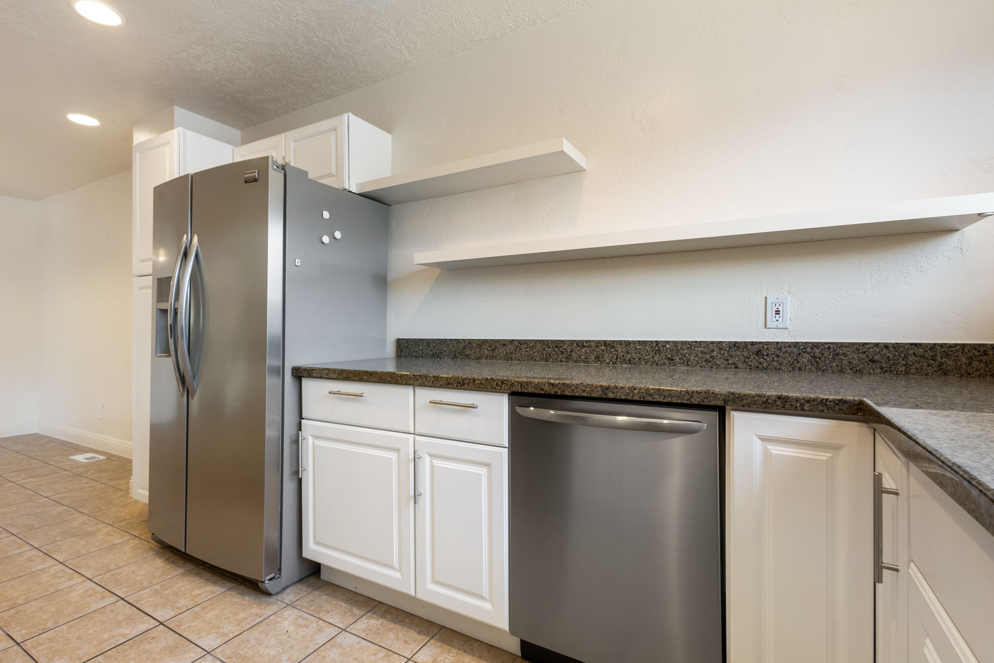 Kitchen featuring stainless steel appliances, white cabinetry with silver hardware, speckled countertops, and open shelving
