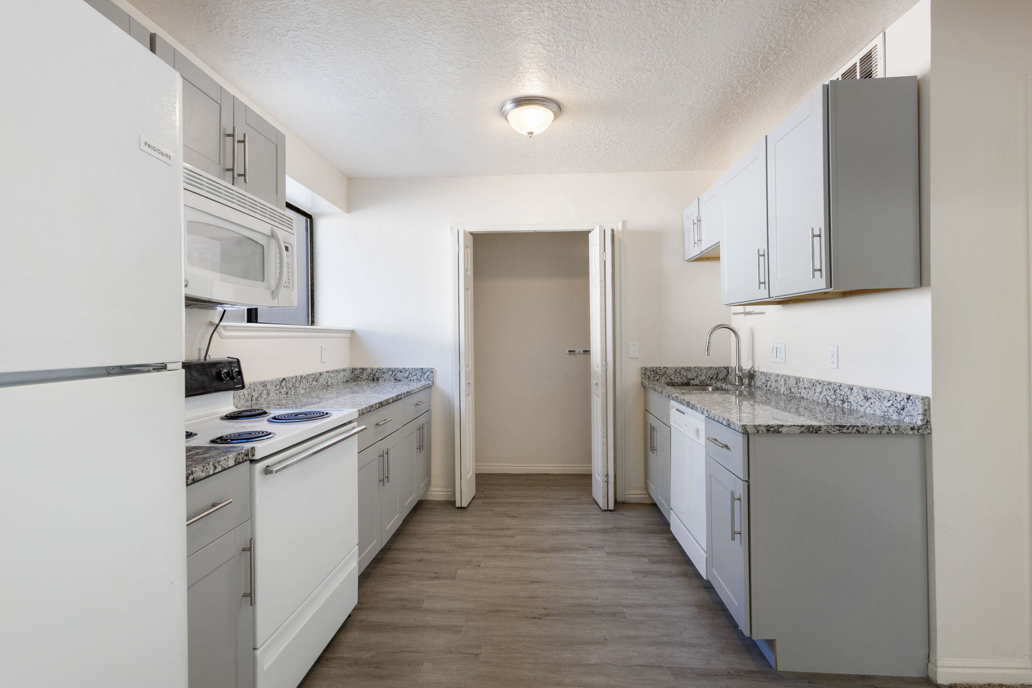 Kitchen featuring gray cabinetry, granite-style countertops, wood-finish flooring, white appliances, and a stainless steel faucet