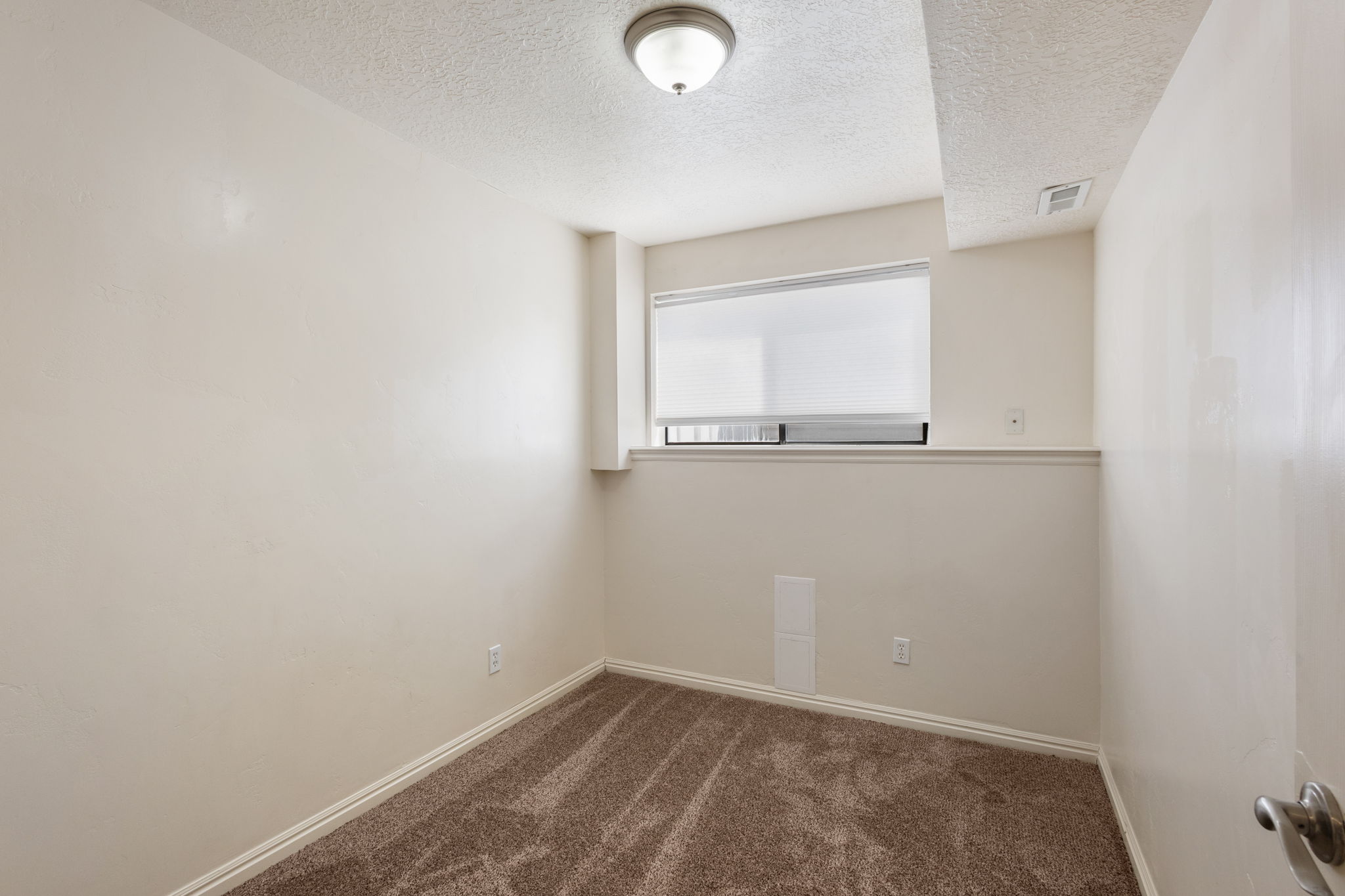 Compact room featuring a single window with blinds, neutral wall paint, textured ceiling, and brown carpet flooring