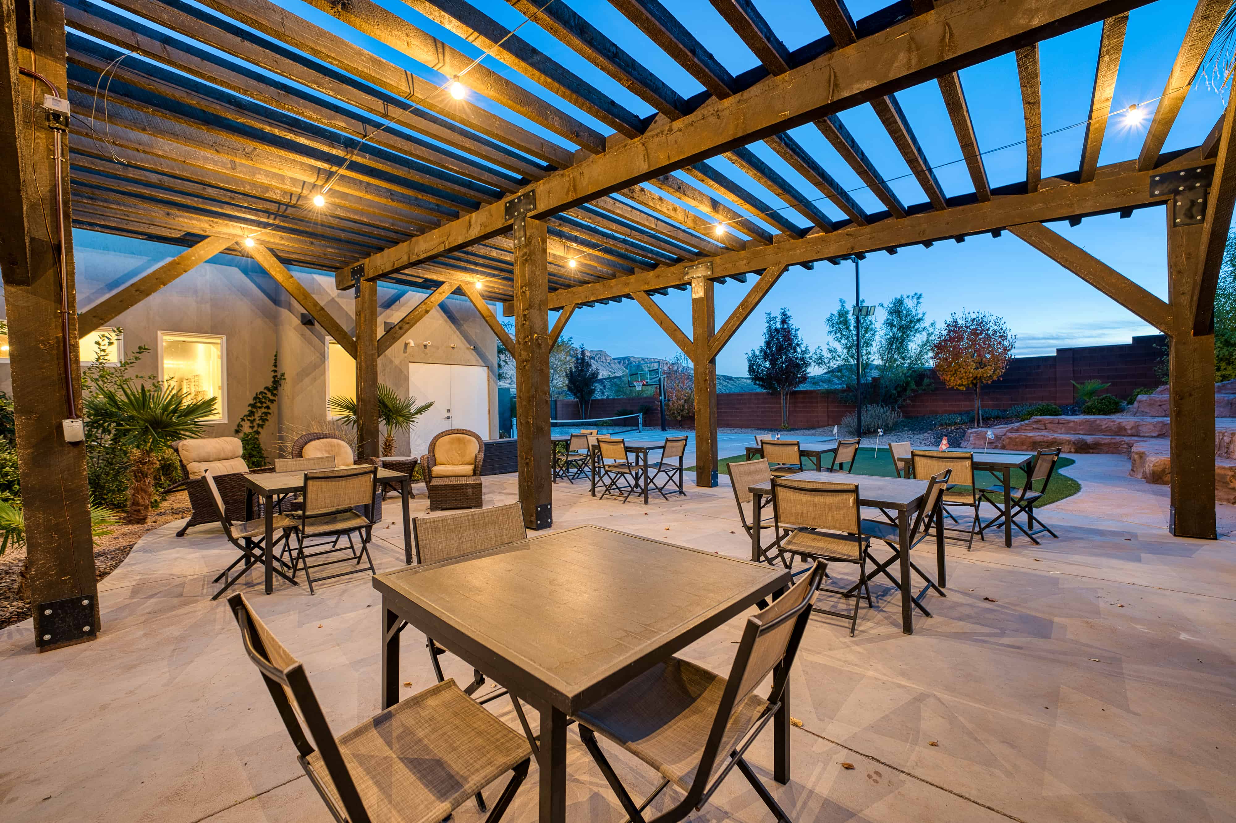 Expansive outdoor patio featuring a wooden pergola, string lighting, paved flooring, and a putting green