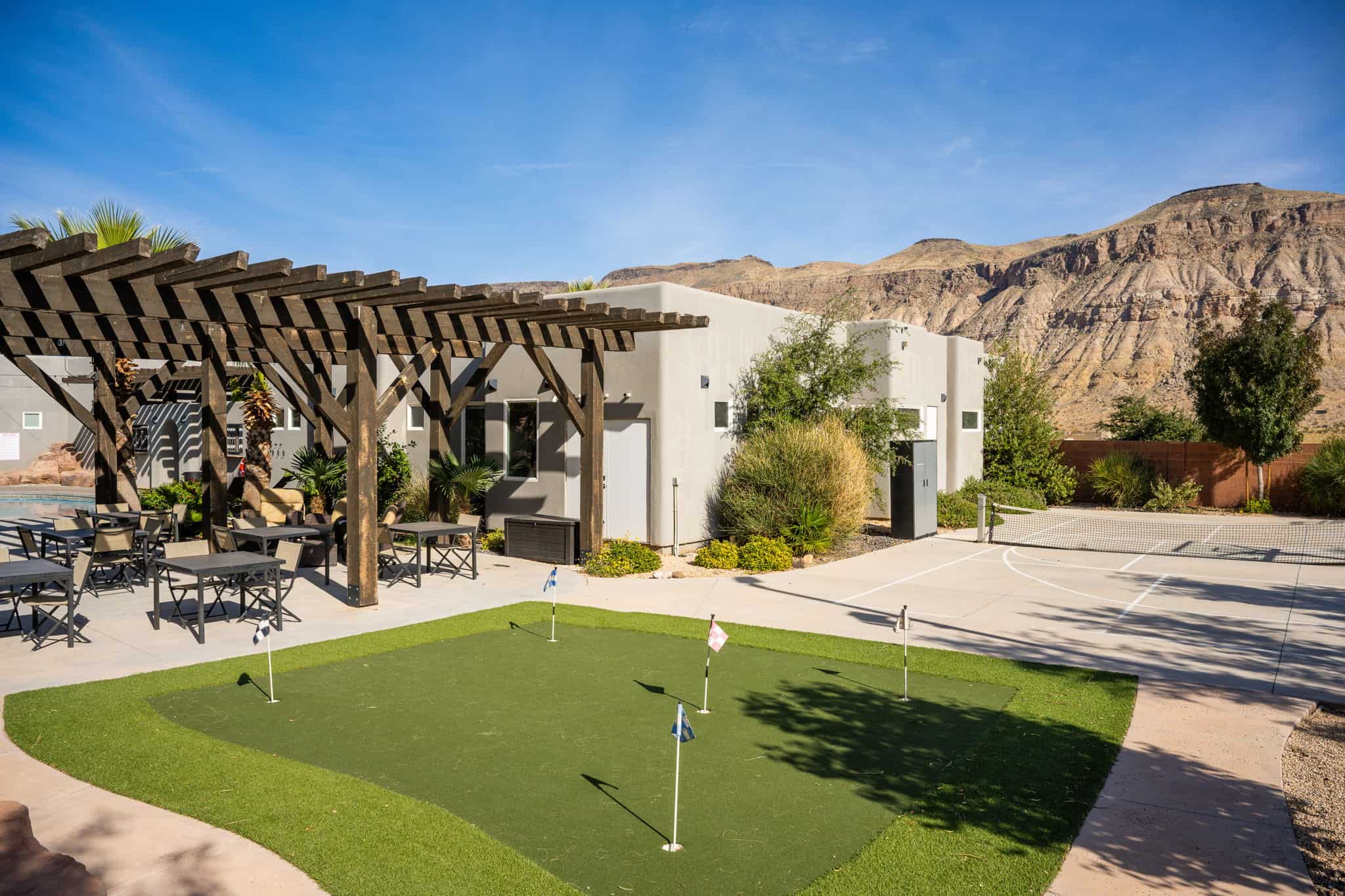 Outdoor putting green with multiple holes, a sports court, and a covered patio area with a wood pergola