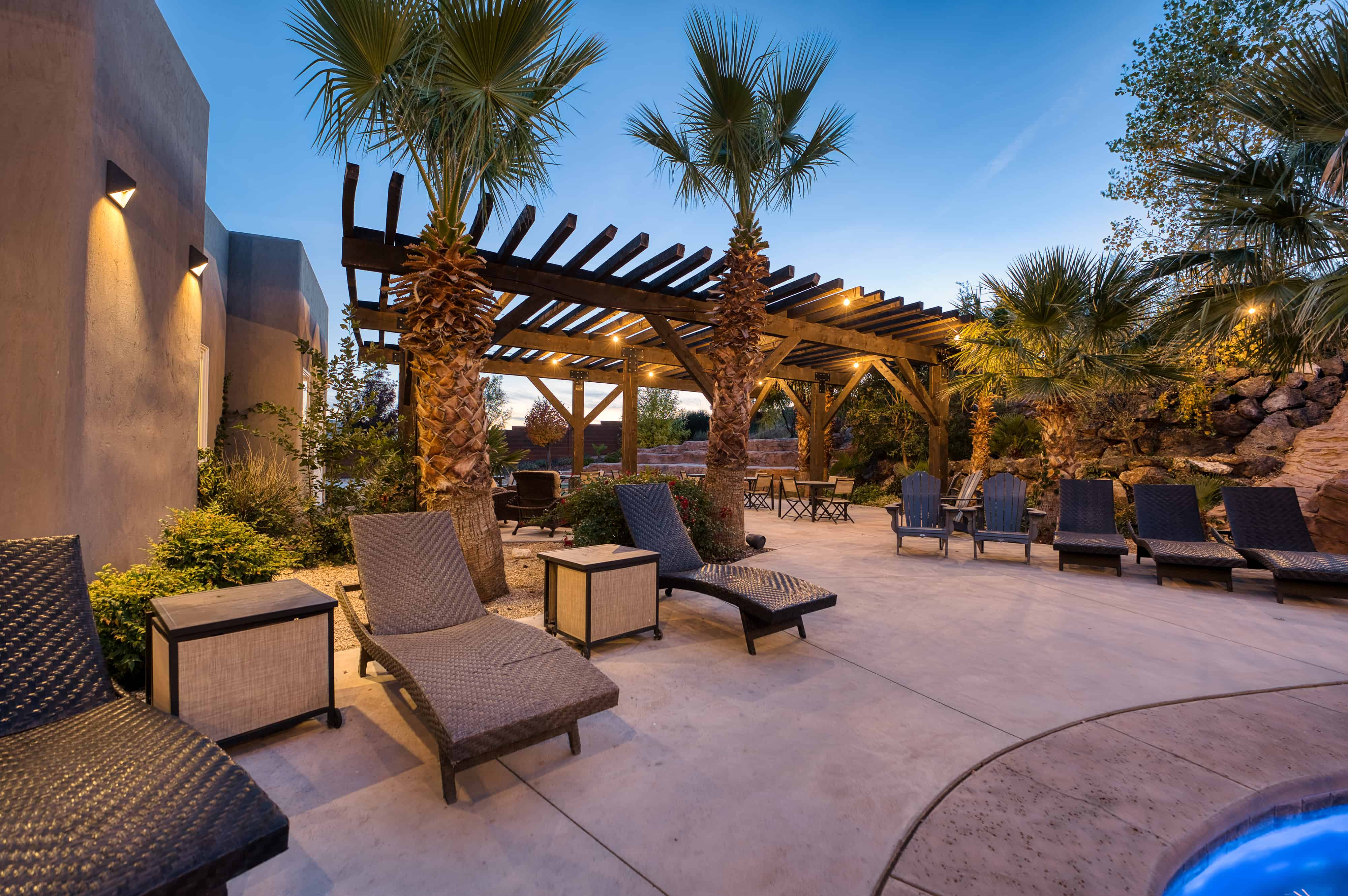 Expansive outdoor patio featuring a large wooden pergola with string lighting, multiple palm trees, and integrated wall sconces