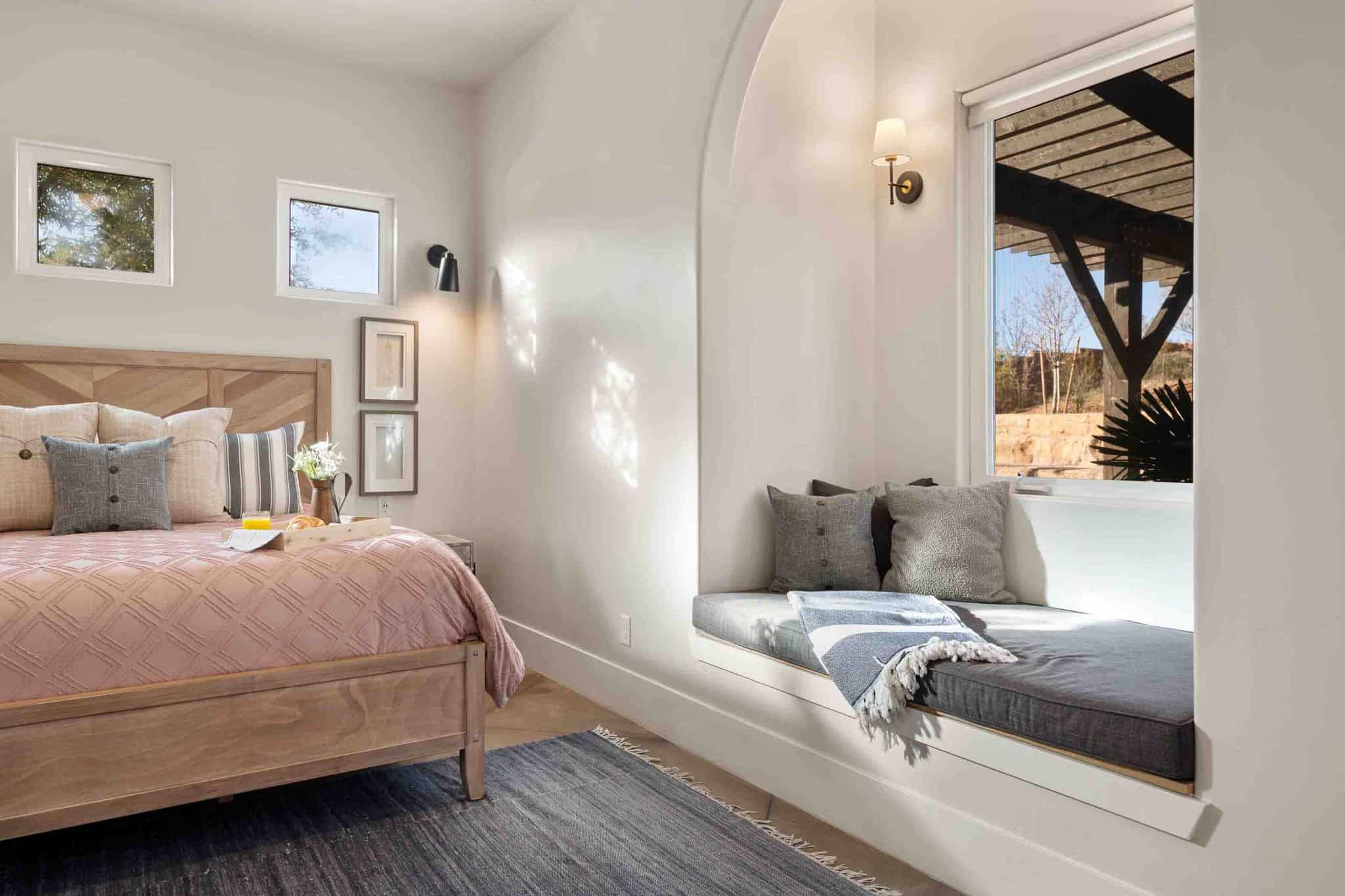 Recessed window seat with integrated lighting, a wood-frame bed, two square windows, a wall-mounted sconce, and neutral wall tones
