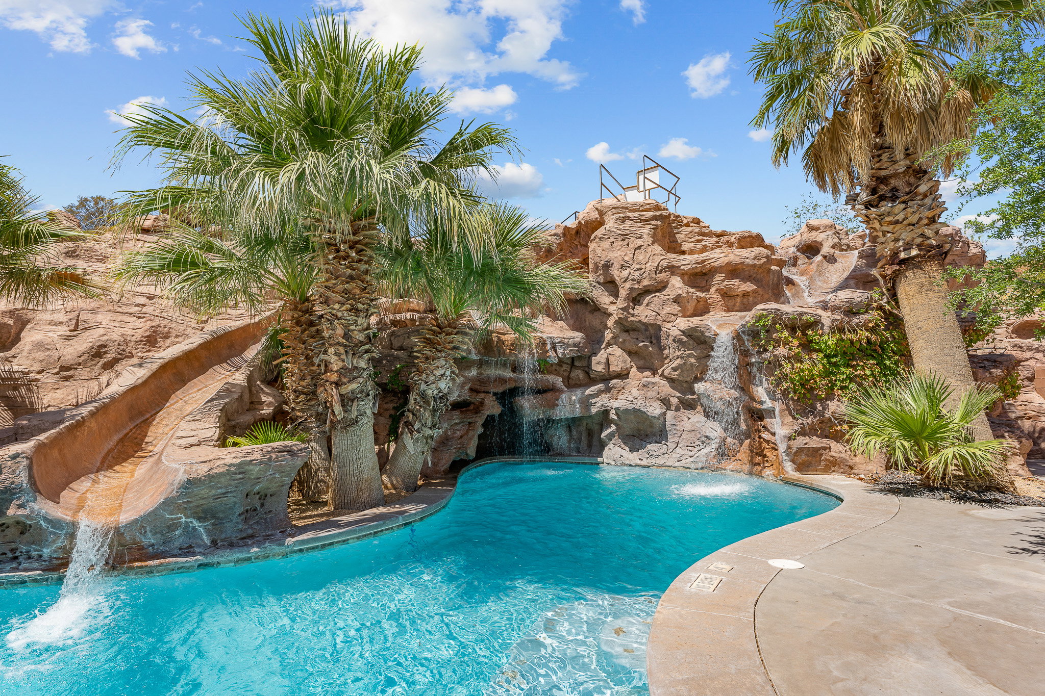 Lagoon-style swimming pool featuring rock formations, multiple waterfalls, a built-in water slide, and mature palm trees
