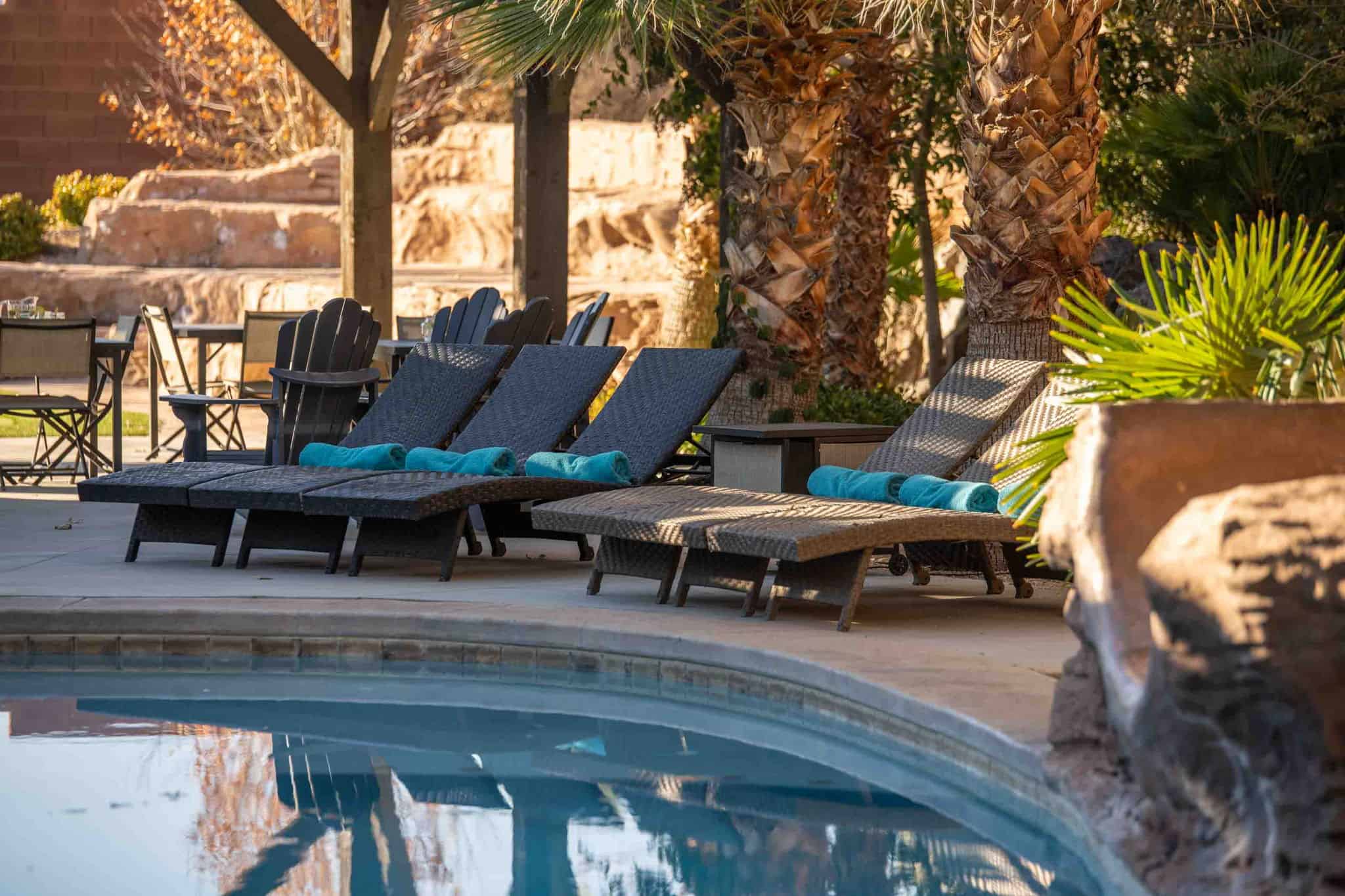 Poolside patio featuring a stone rock feature, mature palm trees, and wood pergola structure