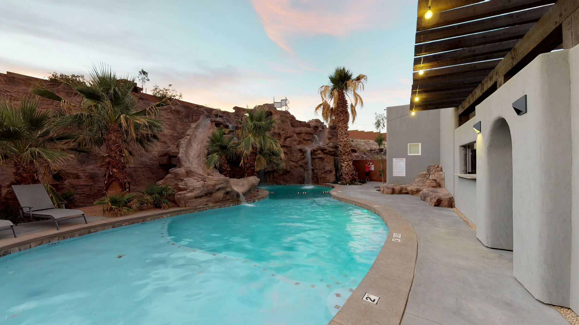 Curved swimming pool featuring a rock waterfall, surrounded by mature palm trees and desert landscaping