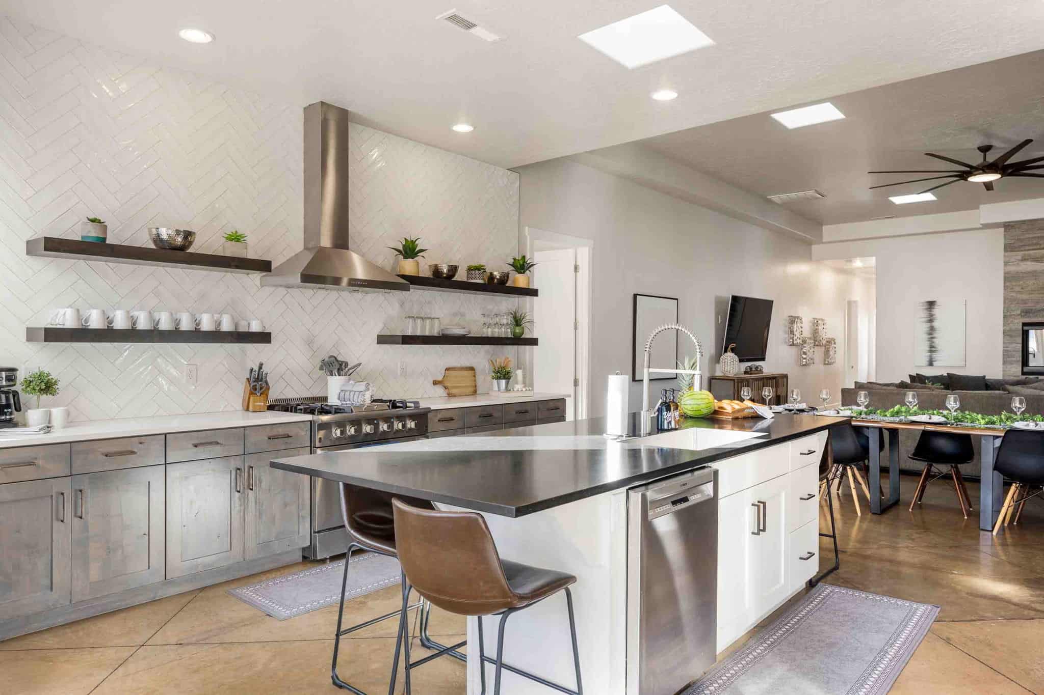 Modern kitchen featuring a large island with sink, stainless steel appliances, white subway tile backsplash in a herringbone pattern, and open shelving