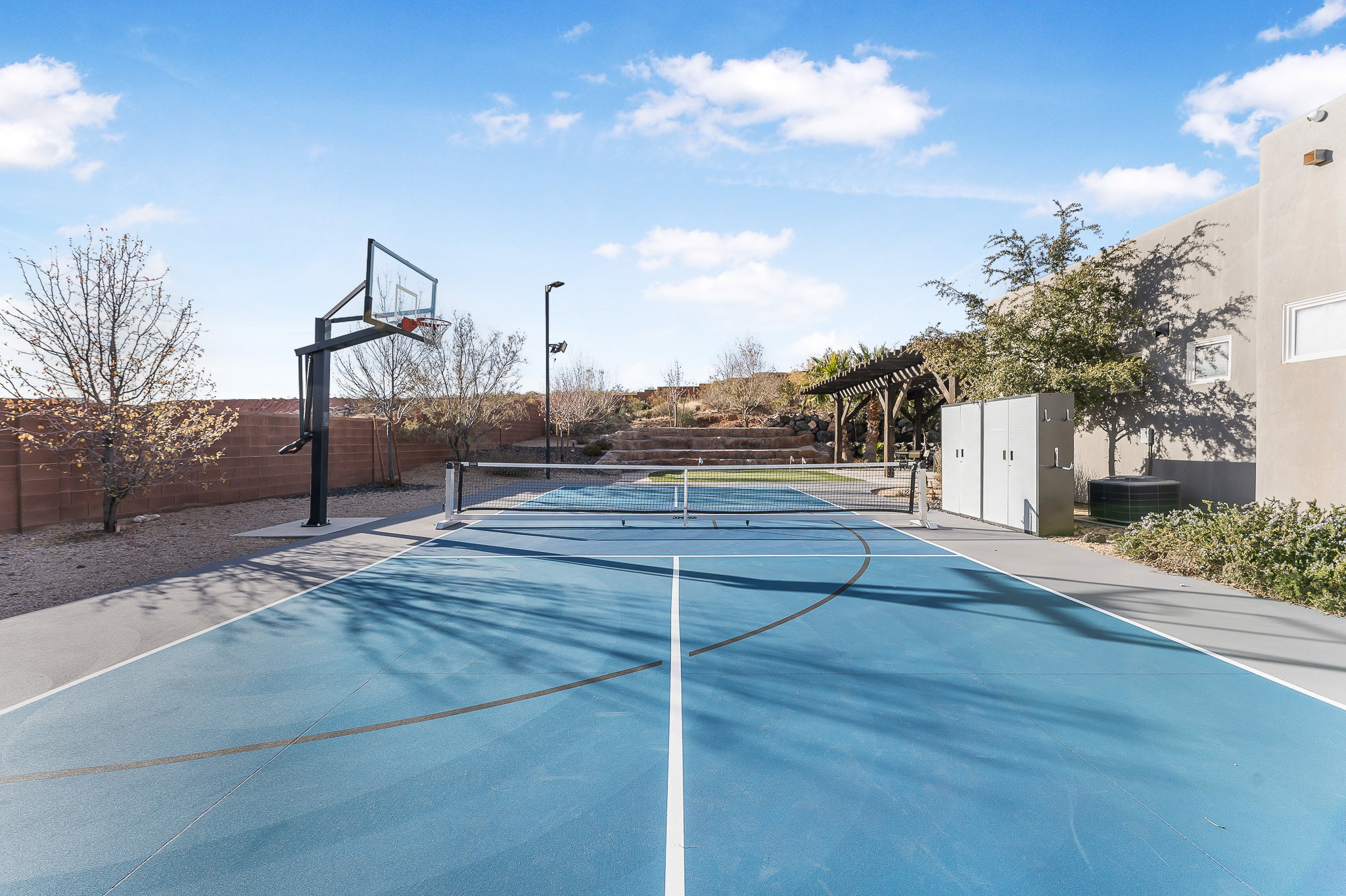 Multi-sport court featuring a basketball hoop and net, alongside a shaded pergola structure