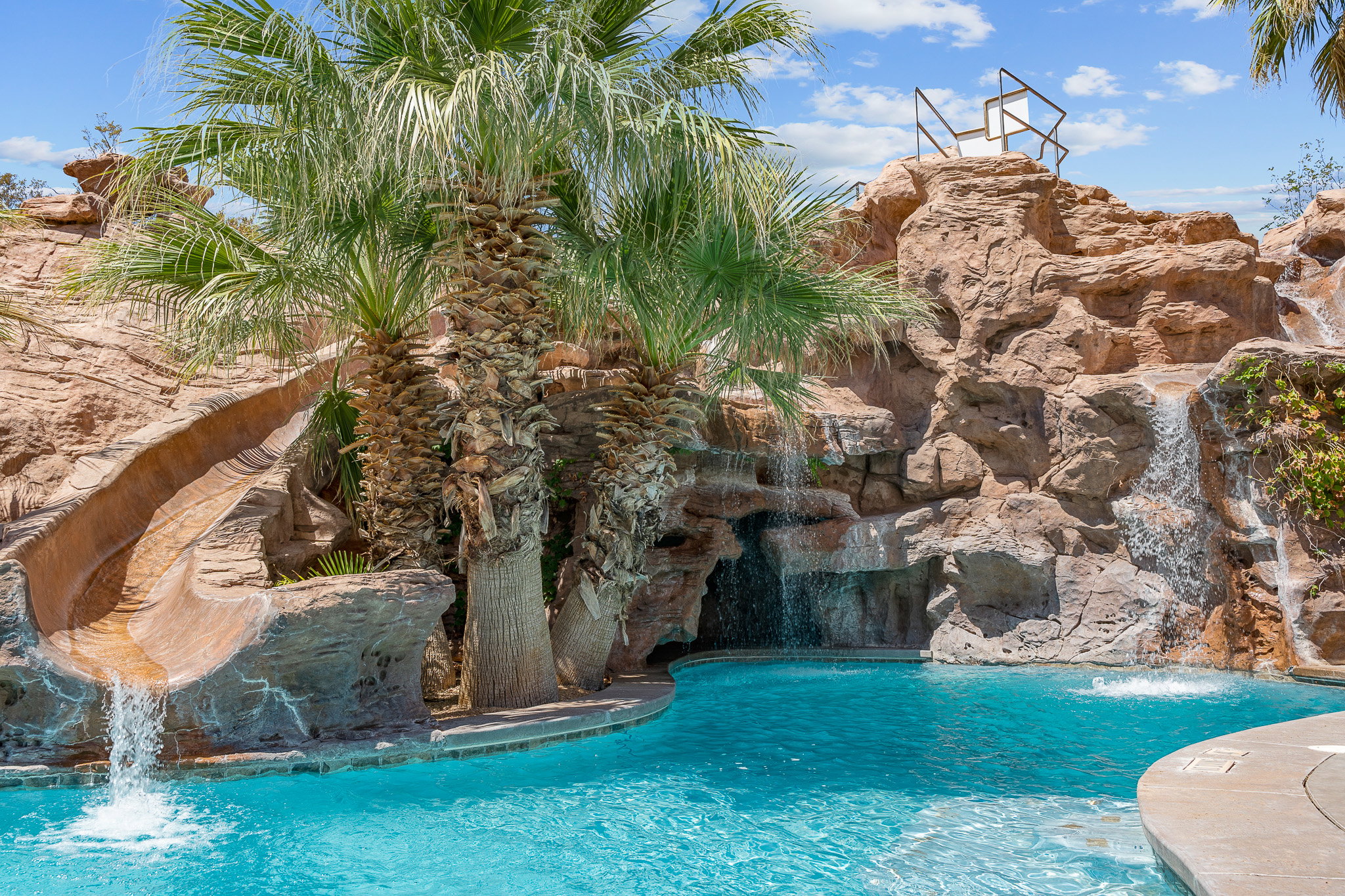 Custom pool with rock grotto, integrated water slide, multiple waterfalls, and established palm trees