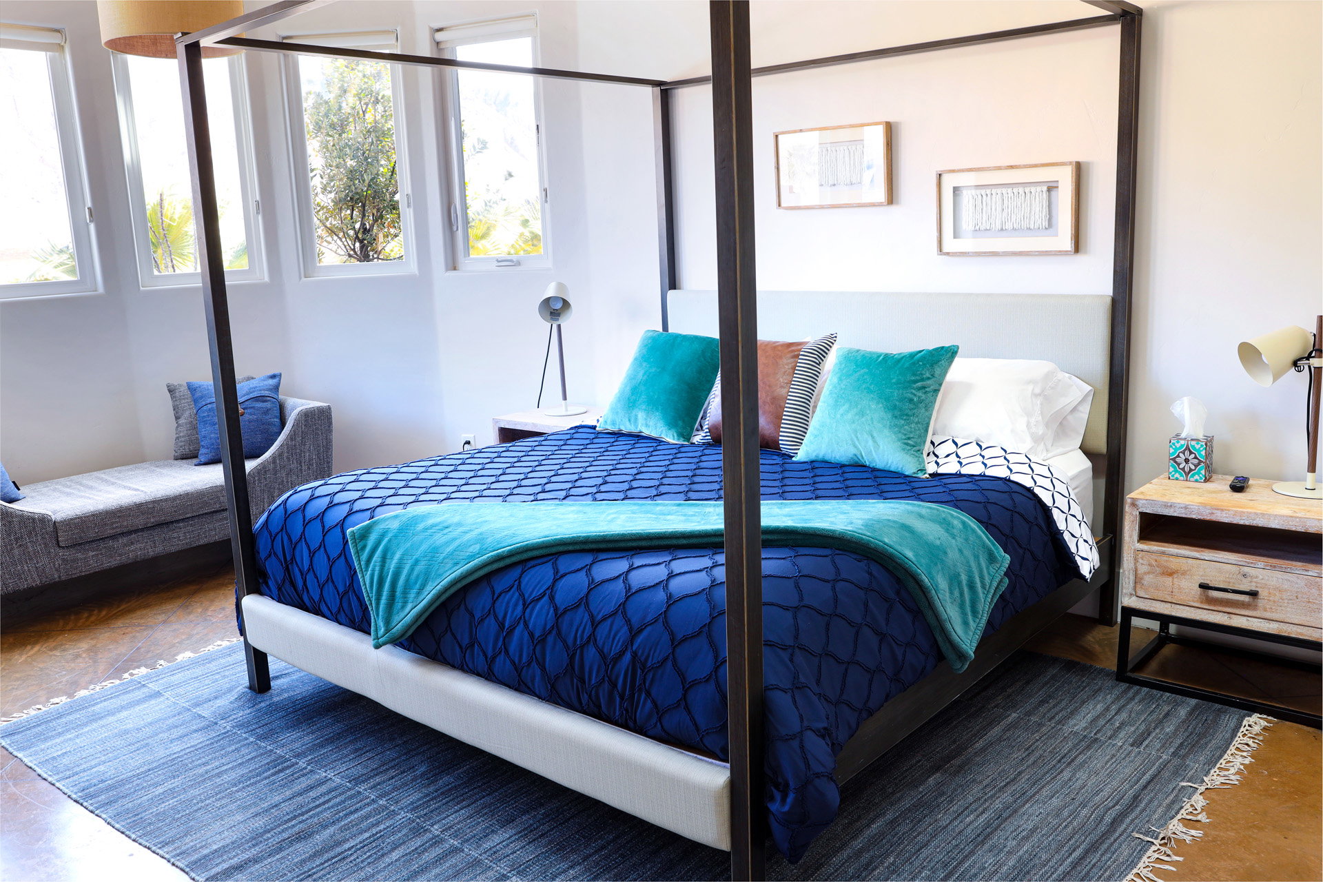 Spacious room featuring multiple large windows, wood-finish flooring, and a contemporary four-poster bed frame