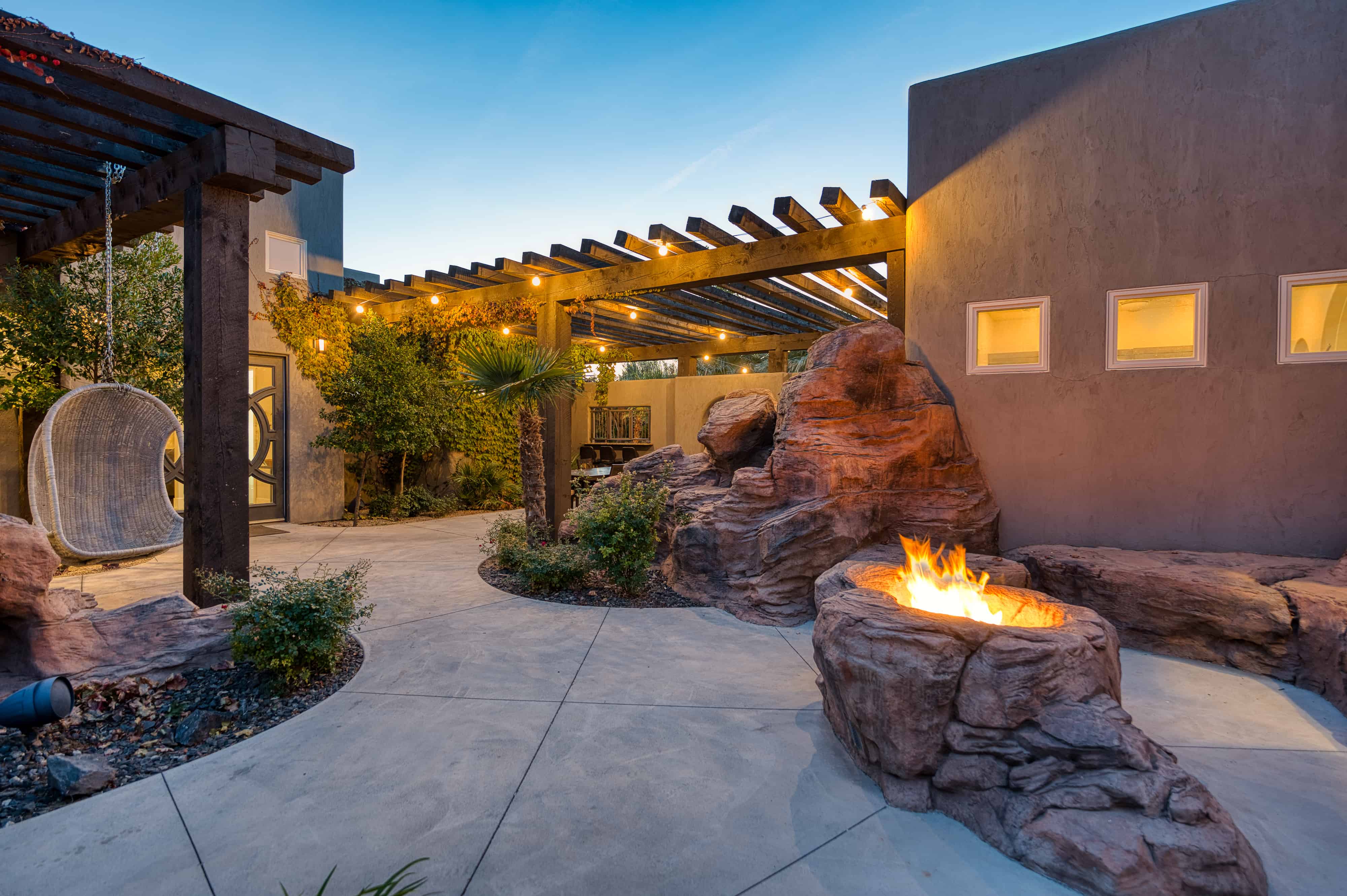 Outdoor patio featuring a rock-formed fire pit, concrete paving, and a wooden pergola with string lighting