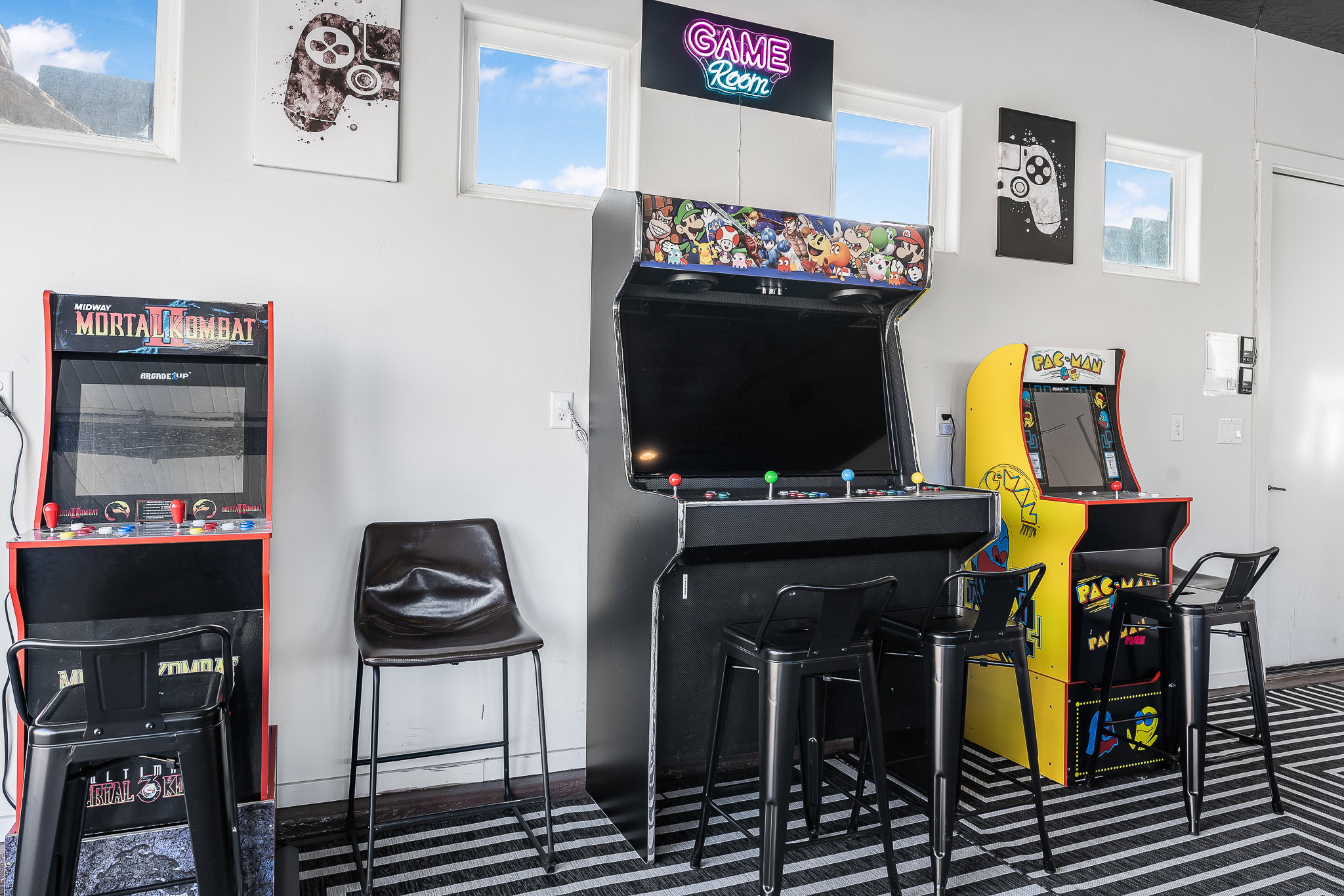 Recreation room featuring a neon "Game Room" sign, multiple arcade cabinets, and large windows