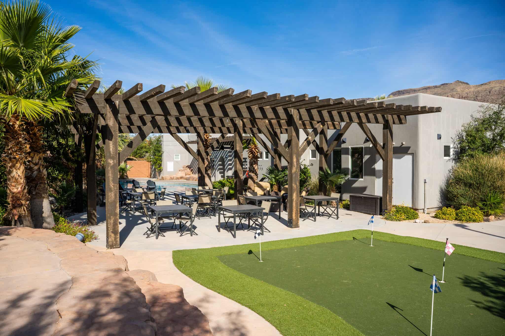 Expansive outdoor area featuring a putting green, a large wood pergola, and a concrete patio