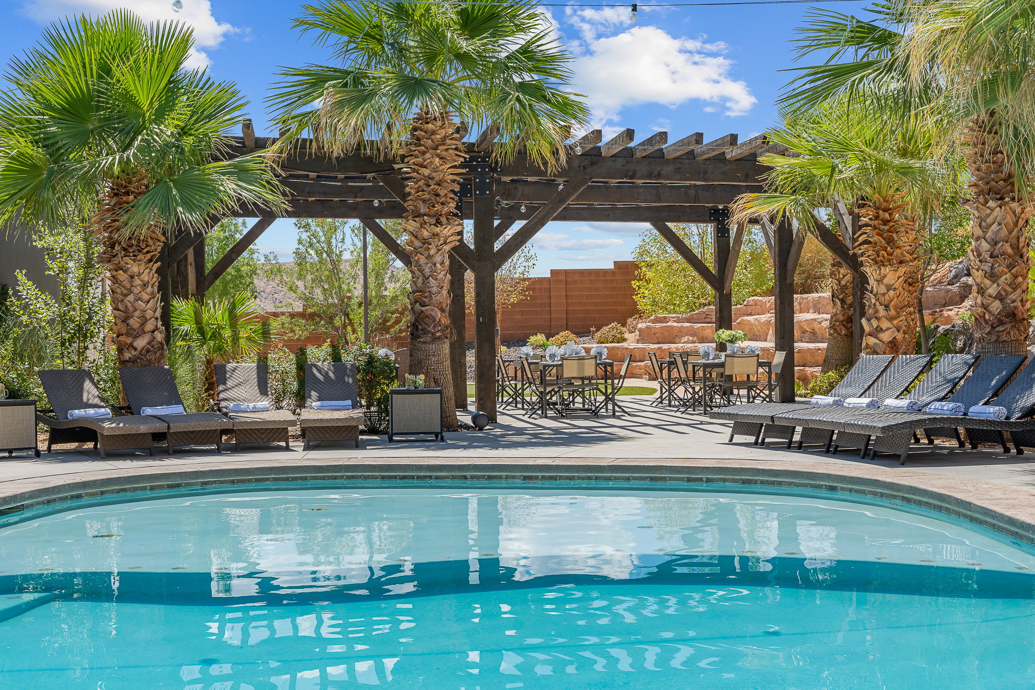 Inviting outdoor pool area featuring a curved swimming pool, a dark wood pergola, and mature palm trees