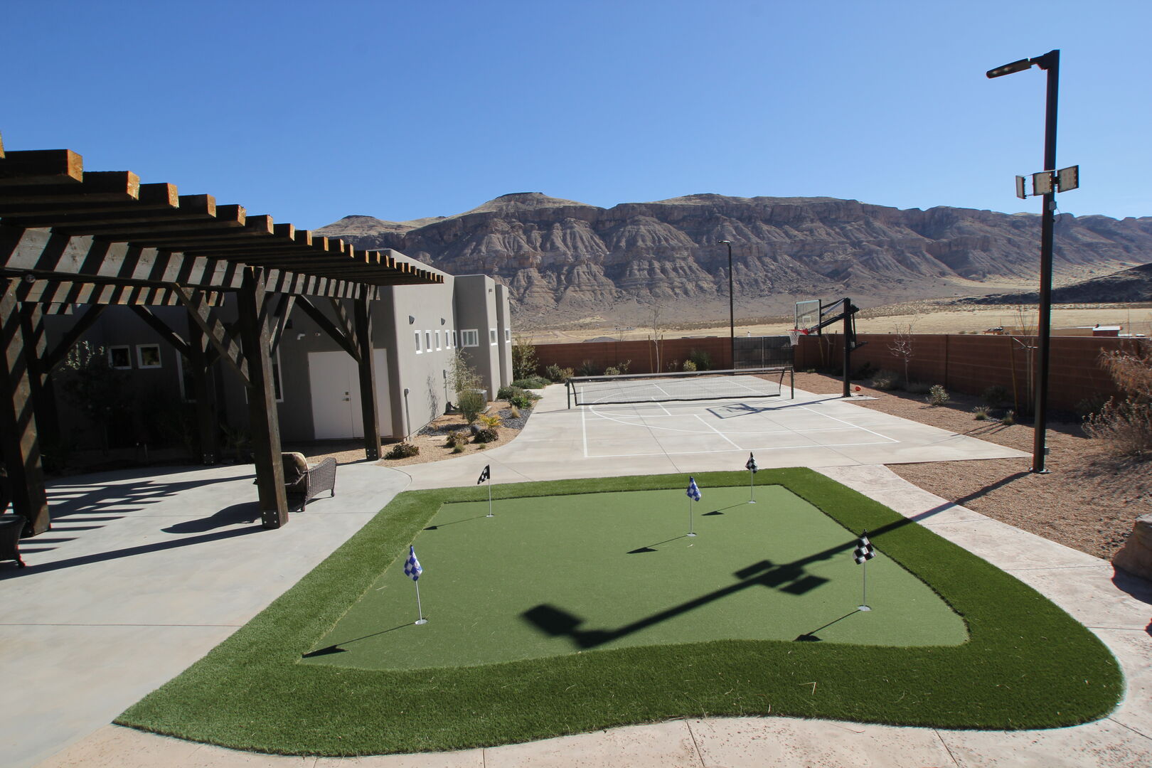 Expansive outdoor entertainment space featuring a putting green, multi-sport court with basketball hoop and net, and a covered pergola