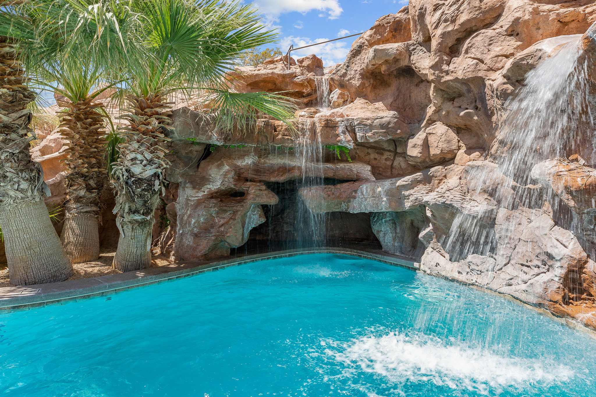 Resort-style pool featuring a rock waterfall, grotto, and mature palm trees