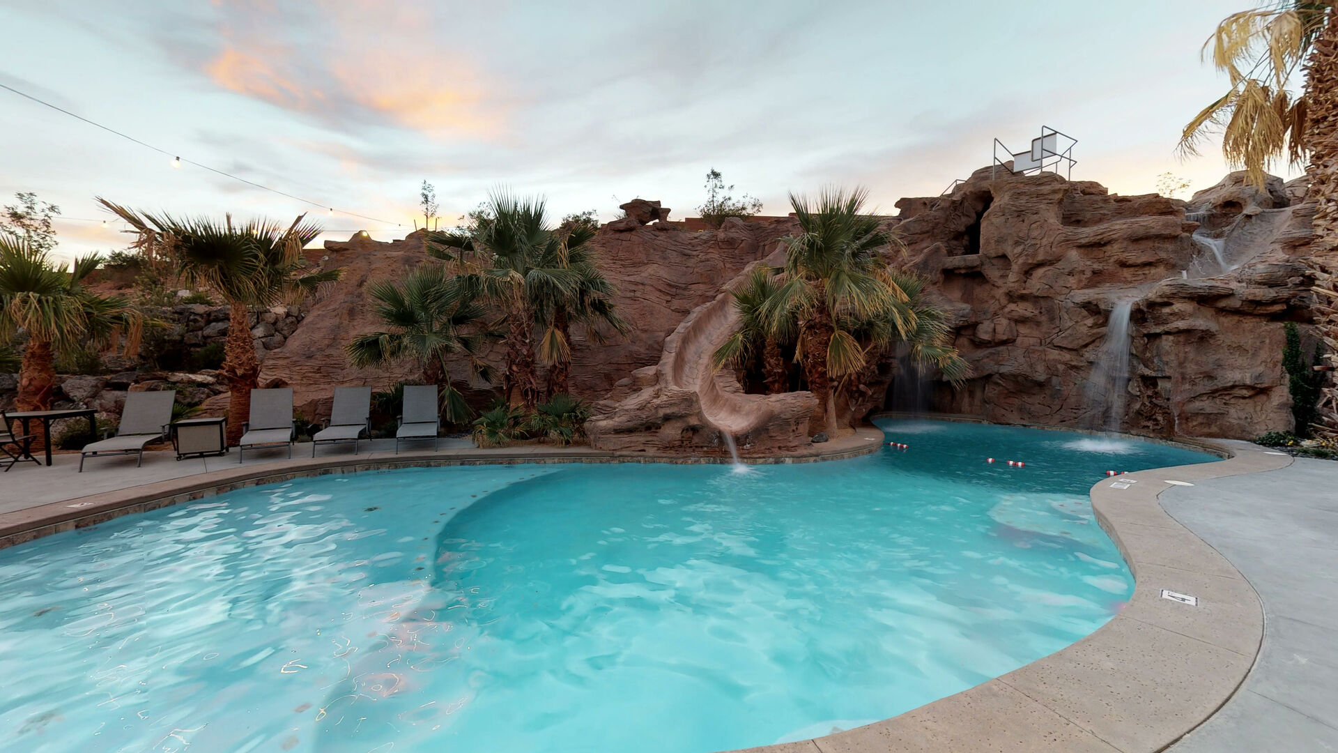 Resort-style pool area featuring a rock waterfall, integrated water slide, and surrounding rock formations