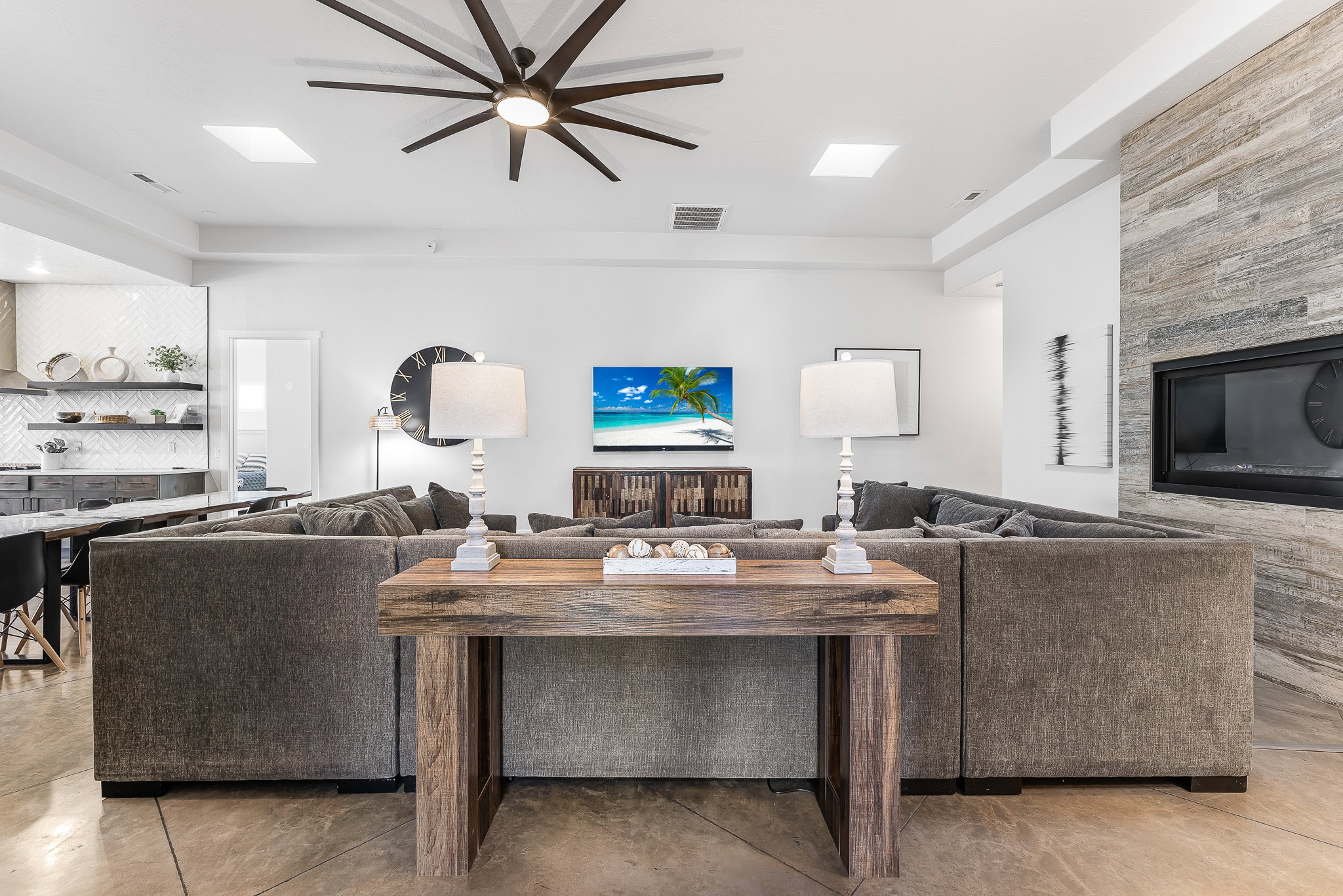 Great room featuring a contemporary ceiling fan with integrated lighting, skylights, and a recessed fireplace with a stacked stone surround