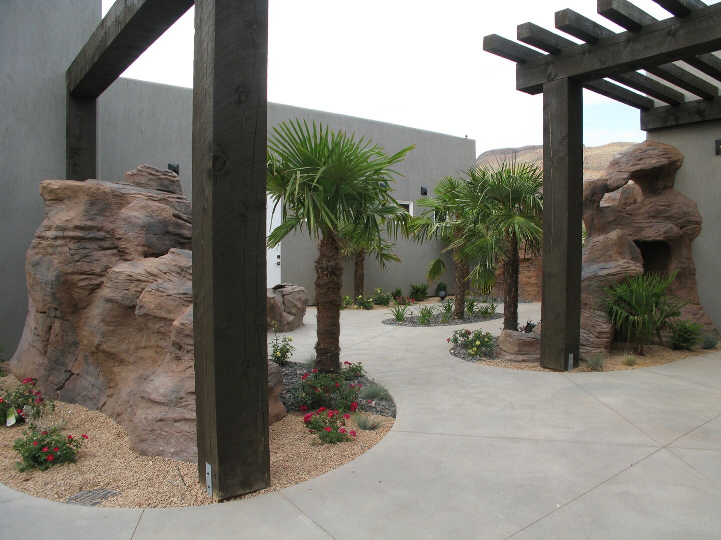 Landscaped courtyard featuring mature palm trees, rock formations, and gravel beds with plantings
