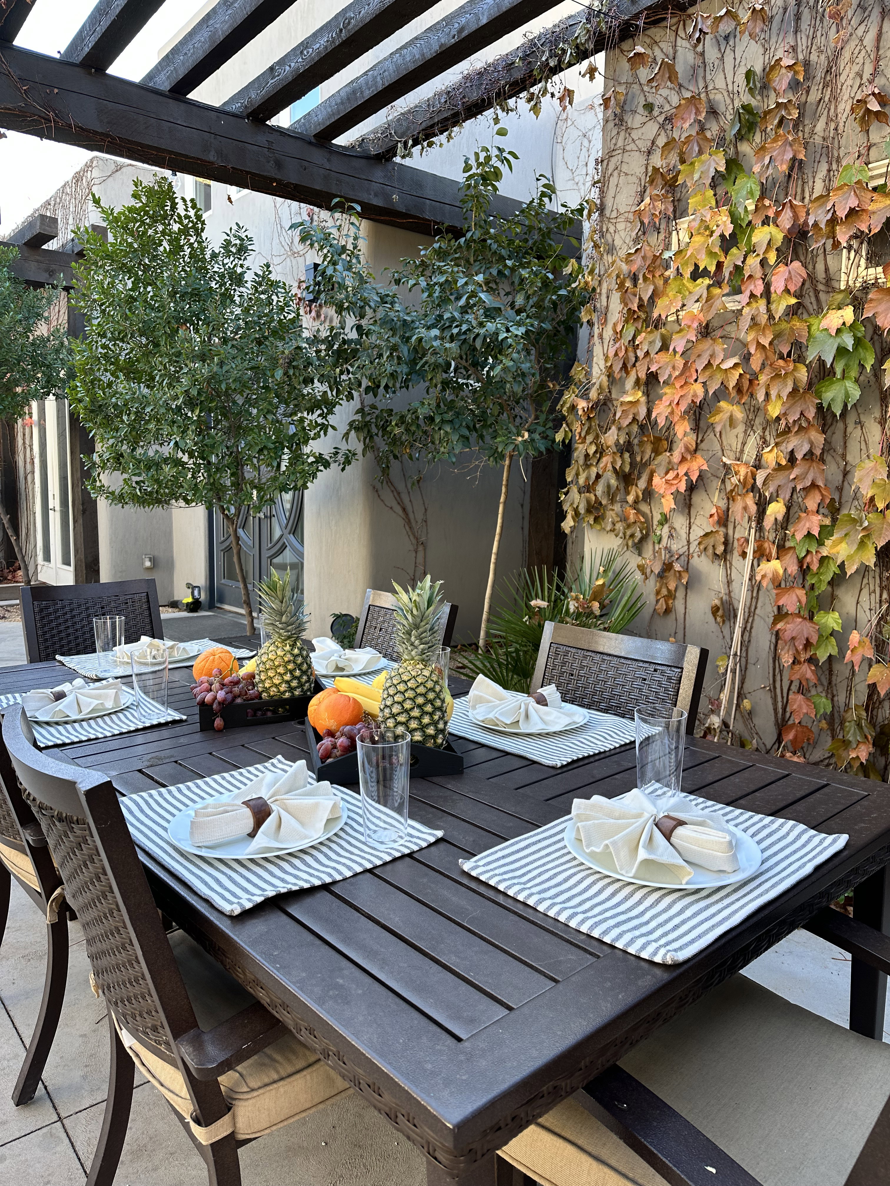 Outdoor dining area featuring a dark wood pergola, a paved patio, and a wall adorned with climbing foliage