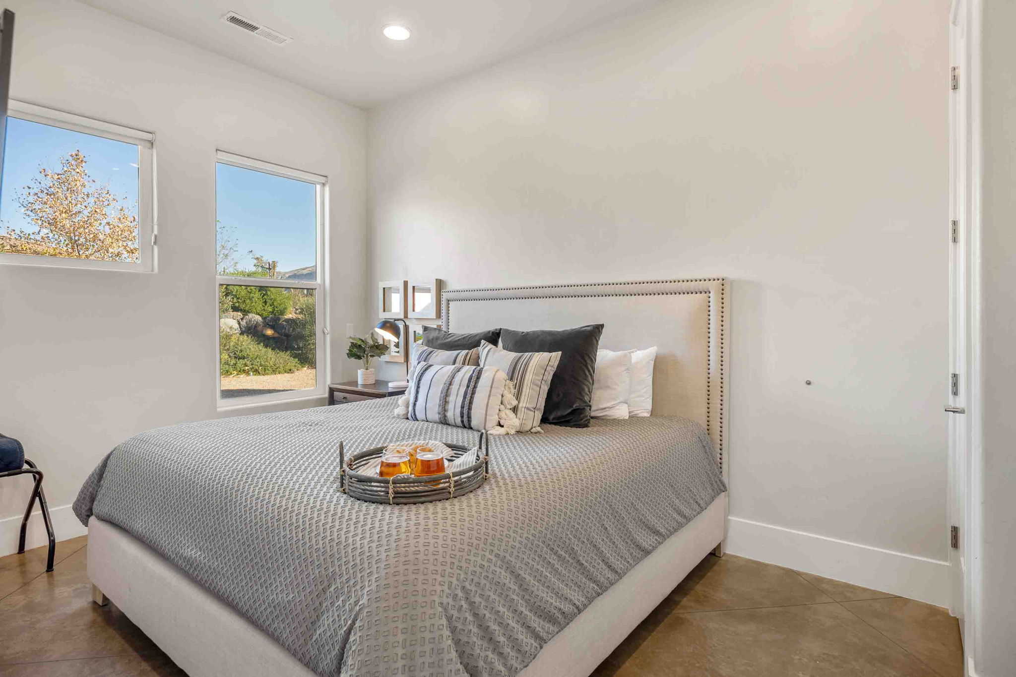 Bedroom featuring two large windows, recessed ceiling lighting, a white painted door, and concrete flooring