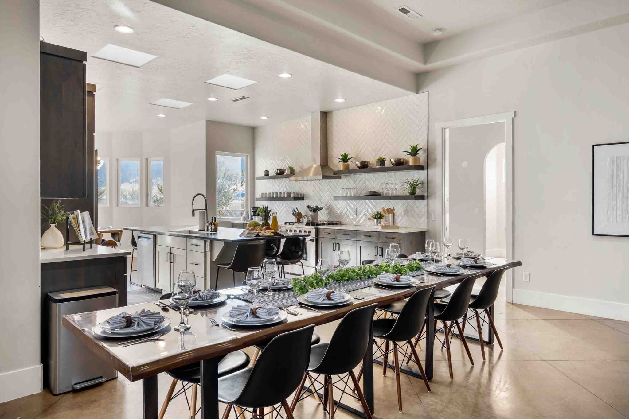 Open-concept kitchen and dining area featuring a herringbone tile backsplash, stainless steel appliances, and a central island with a sink