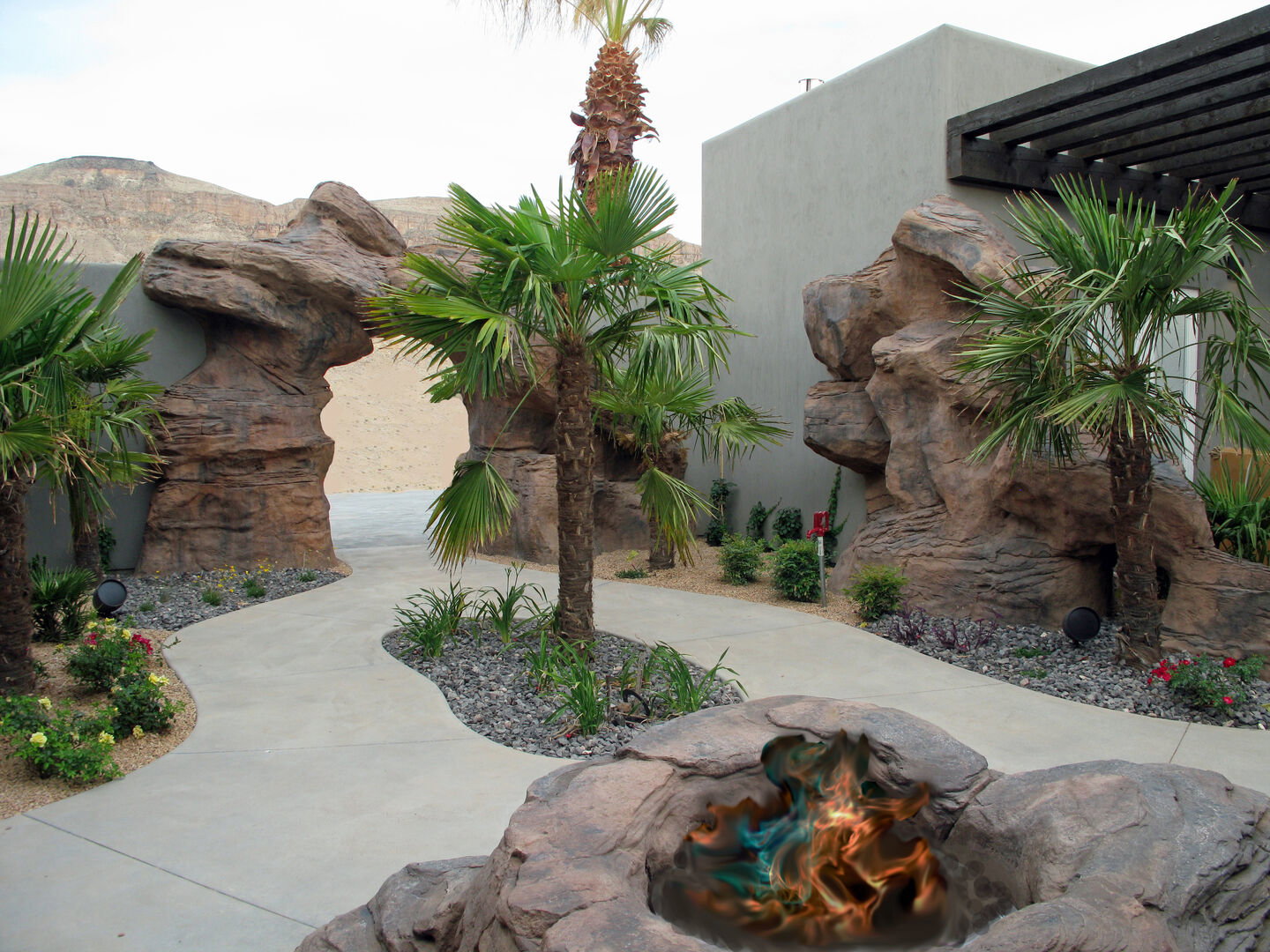 Desert landscaping with a winding concrete pathway, mature palm trees, and rock formations