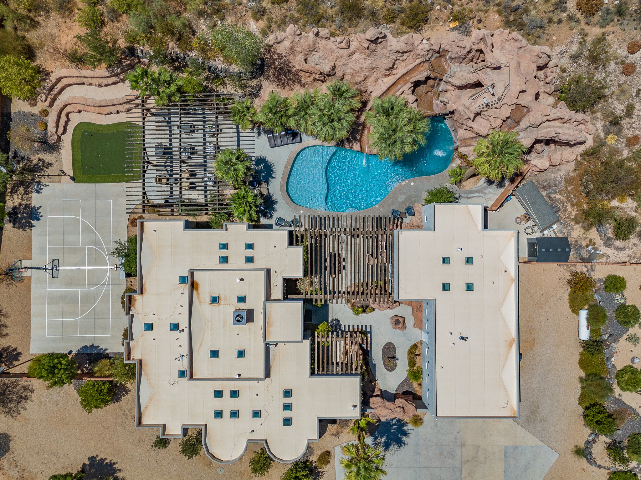 Expansive outdoor amenities featuring a freeform swimming pool with rock waterfall, full basketball court, putting green, and multiple shaded patio areas