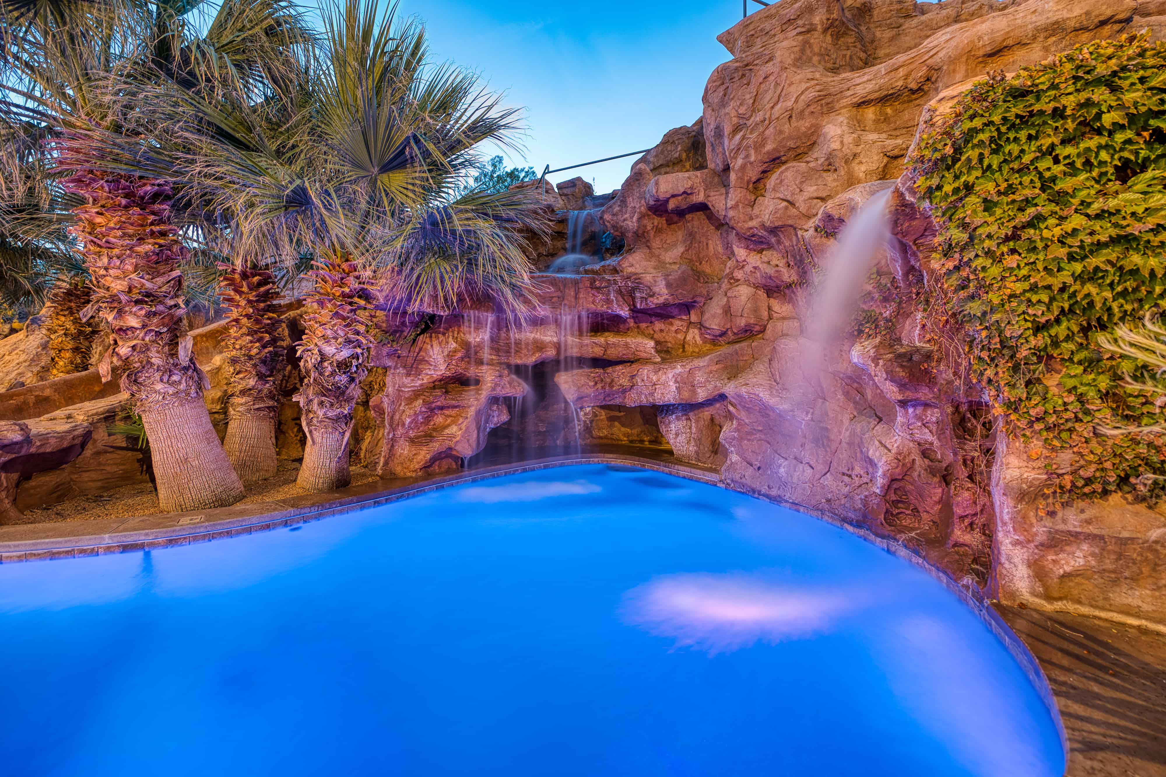 Lagoon-style pool featuring integrated rock waterfall, lush tropical plantings, and a stone-clad grotto