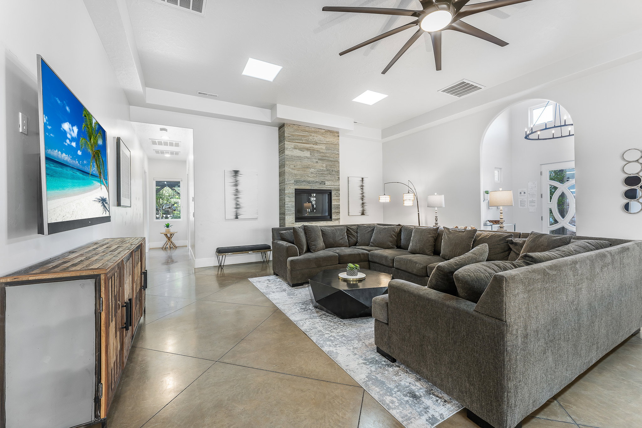 Expansive living space featuring polished concrete flooring, a natural stone-clad fireplace, and recessed ceiling lighting