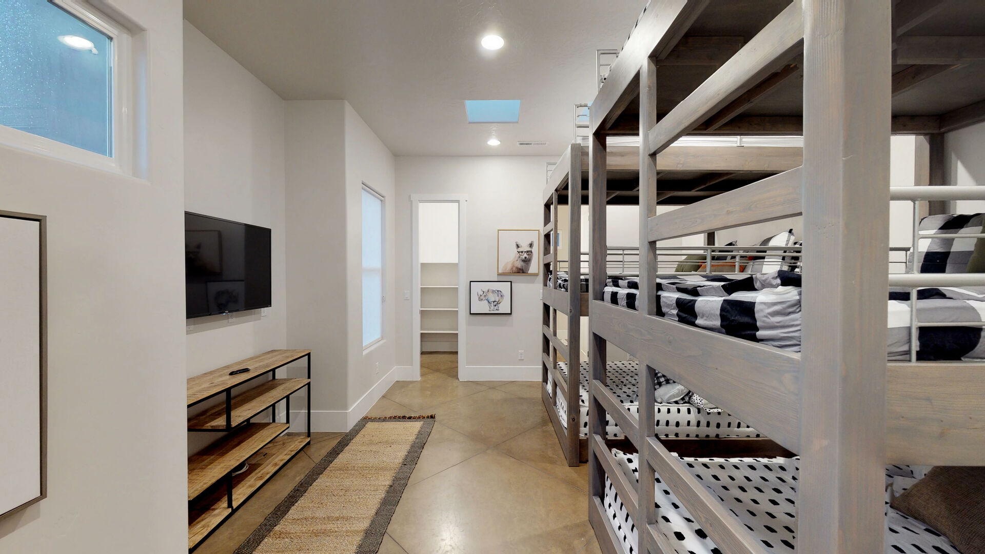 Room featuring multiple stacked bunk beds with wood-finish frames, a wall-mounted television, and a wood-finish media console
