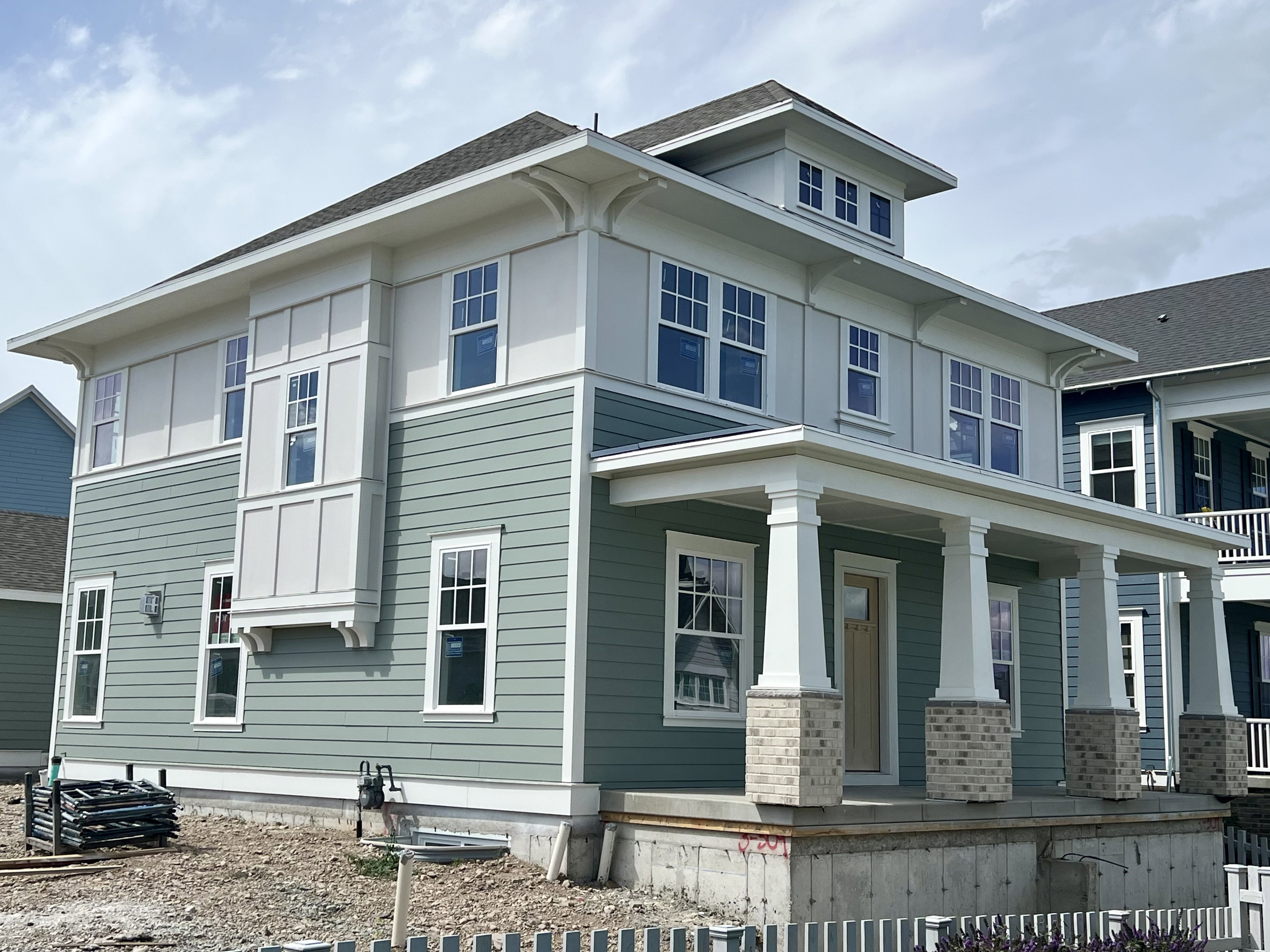 New construction home featuring a light green and white exterior with multiple large windows