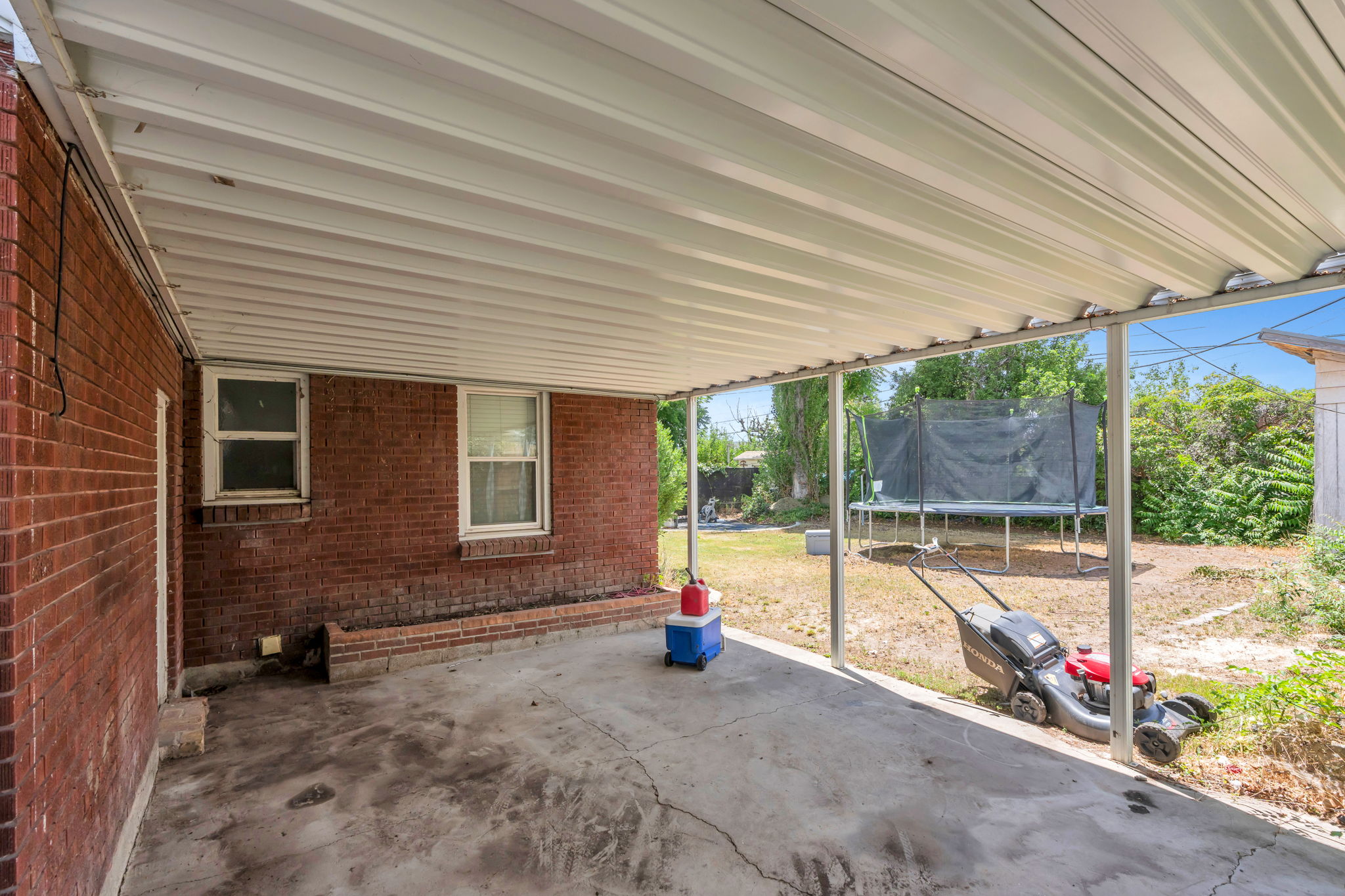 Covered concrete patio with a corrugated metal roof, supported by metal posts