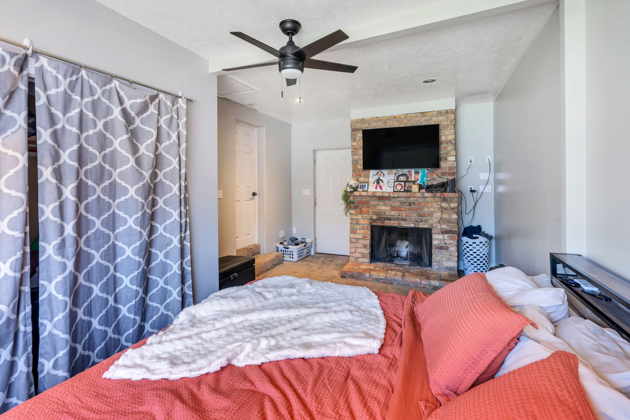Interior room featuring a brick fireplace with a mounted television, a ceiling fan with integrated lighting, and light gray painted walls