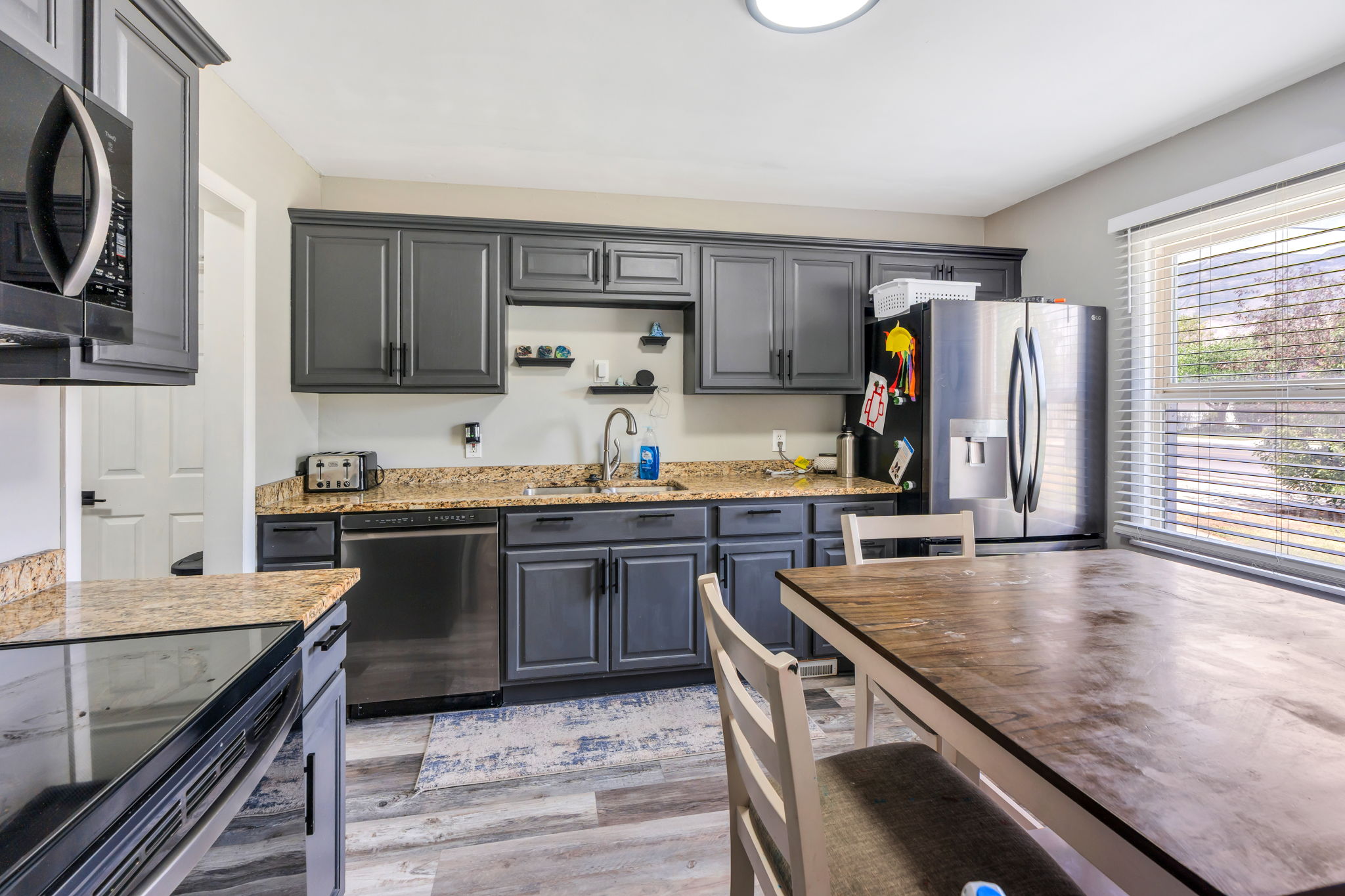 Kitchen featuring dark gray cabinetry, light-toned countertops, stainless steel appliances, and wood-finish flooring