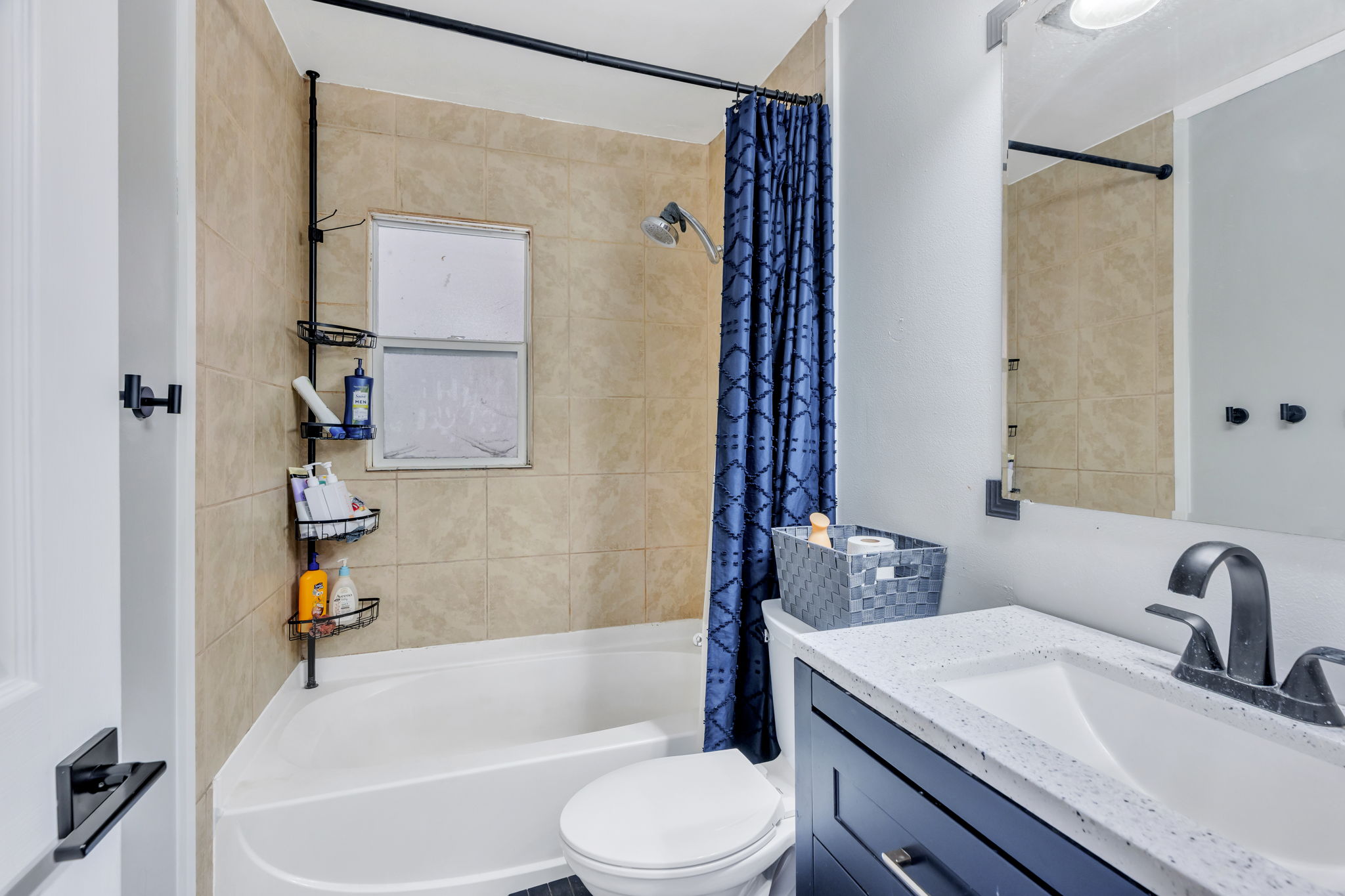 Full bathroom featuring a tub-shower combination with tiled surround, a window, and a vanity with a white countertop and dark base