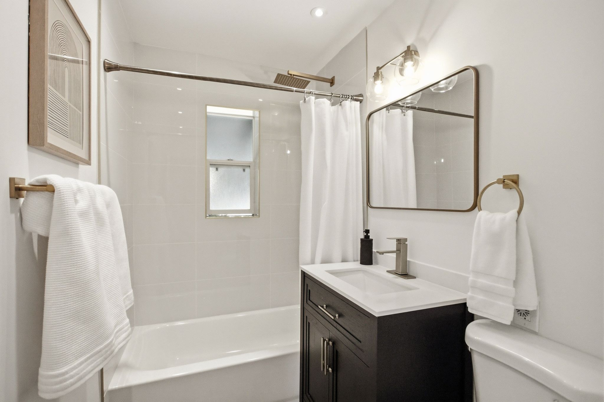 Bathroom featuring a white subway tile shower surround, contemporary vanity with white countertop, rectangular mirror with metallic frame, and modern light fixture