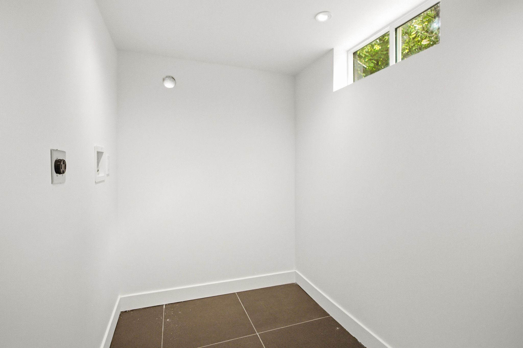 Dedicated laundry area featuring modern floor tiling, a high transom window, and recessed ceiling lighting