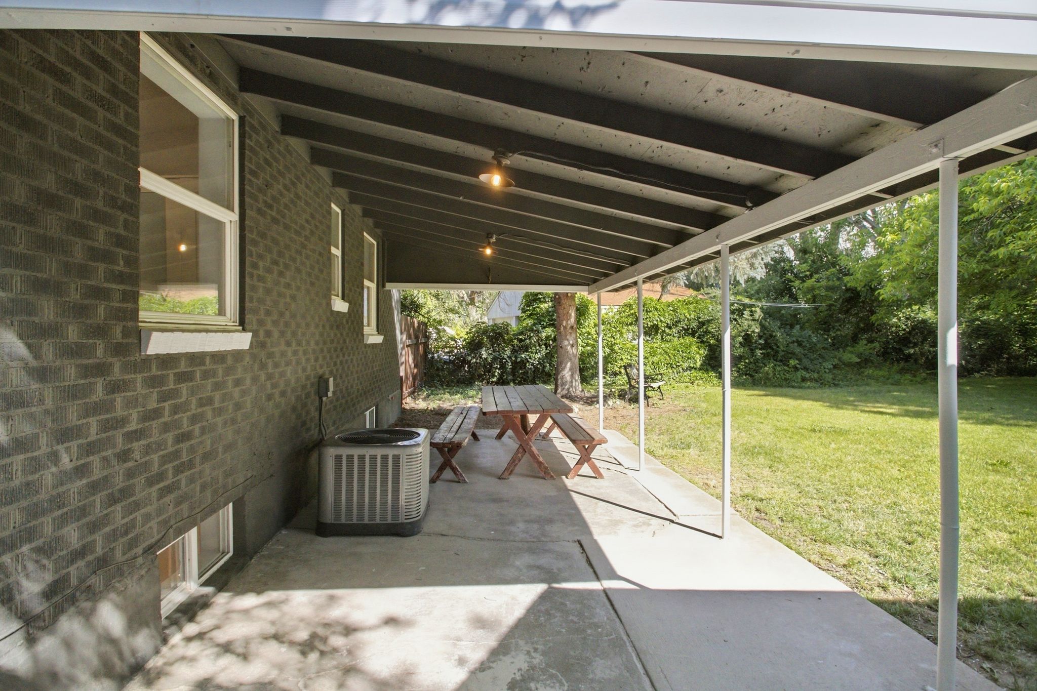 Expansive covered patio featuring a concrete surface, supported by white metal posts, and equipped with overhead lighting
