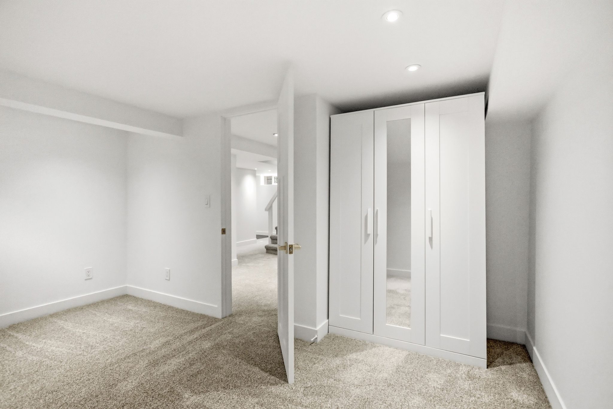 Carpeted room with white walls, recessed lighting, and a built-in white wardrobe featuring mirrored doors and brushed nickel hardware