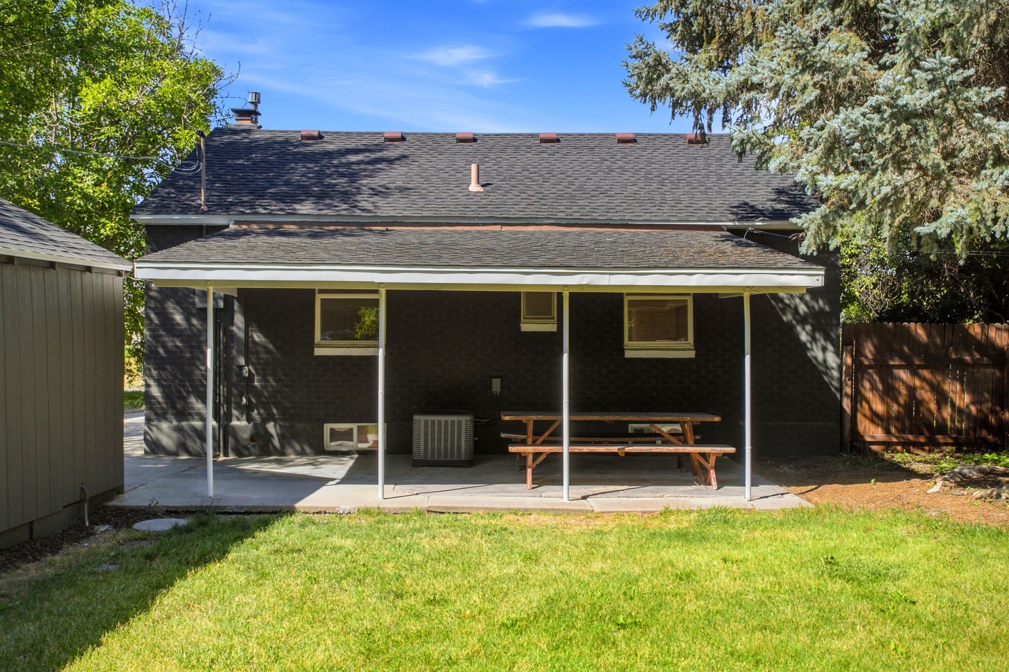 Backyard featuring a covered concrete patio, an expansive lawn area, mature trees, and a separate storage shed