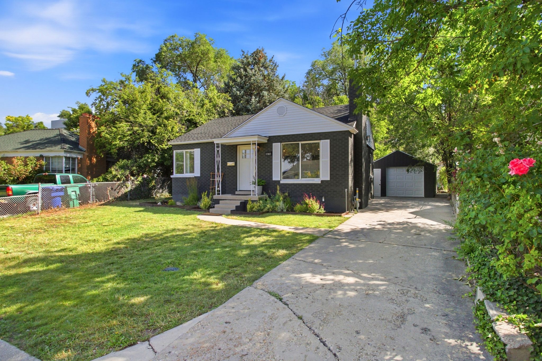 Single-family residence featuring a dark-toned brick exterior with white trim, a concrete driveway, a separate garage structure, and a front lawn with mature trees