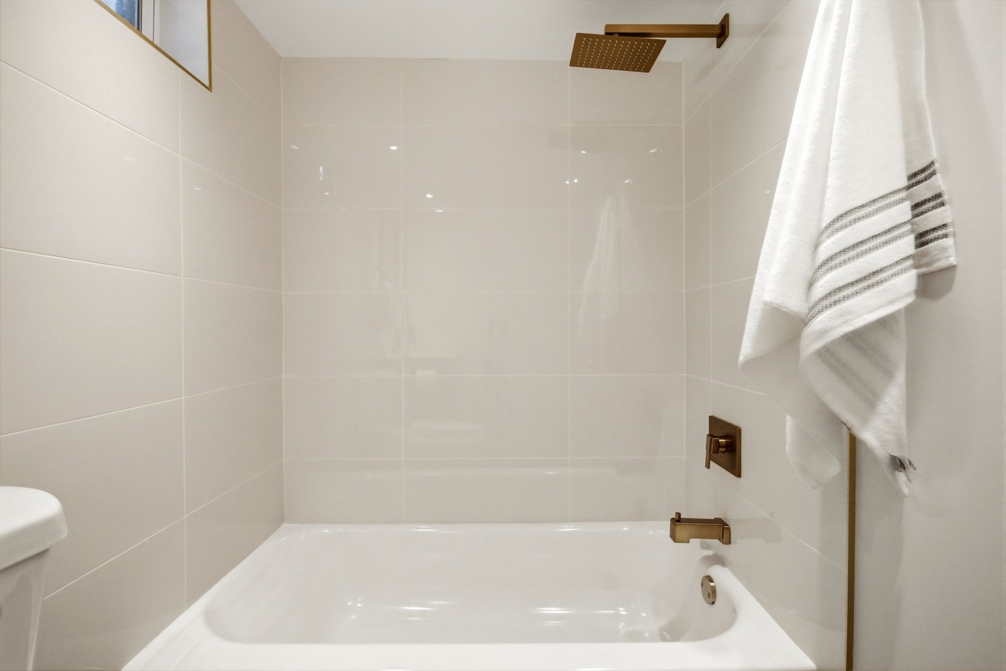 Bathtub with a bronze-finish showerhead, bronze-finish faucet, and glossy white subway tile surround
