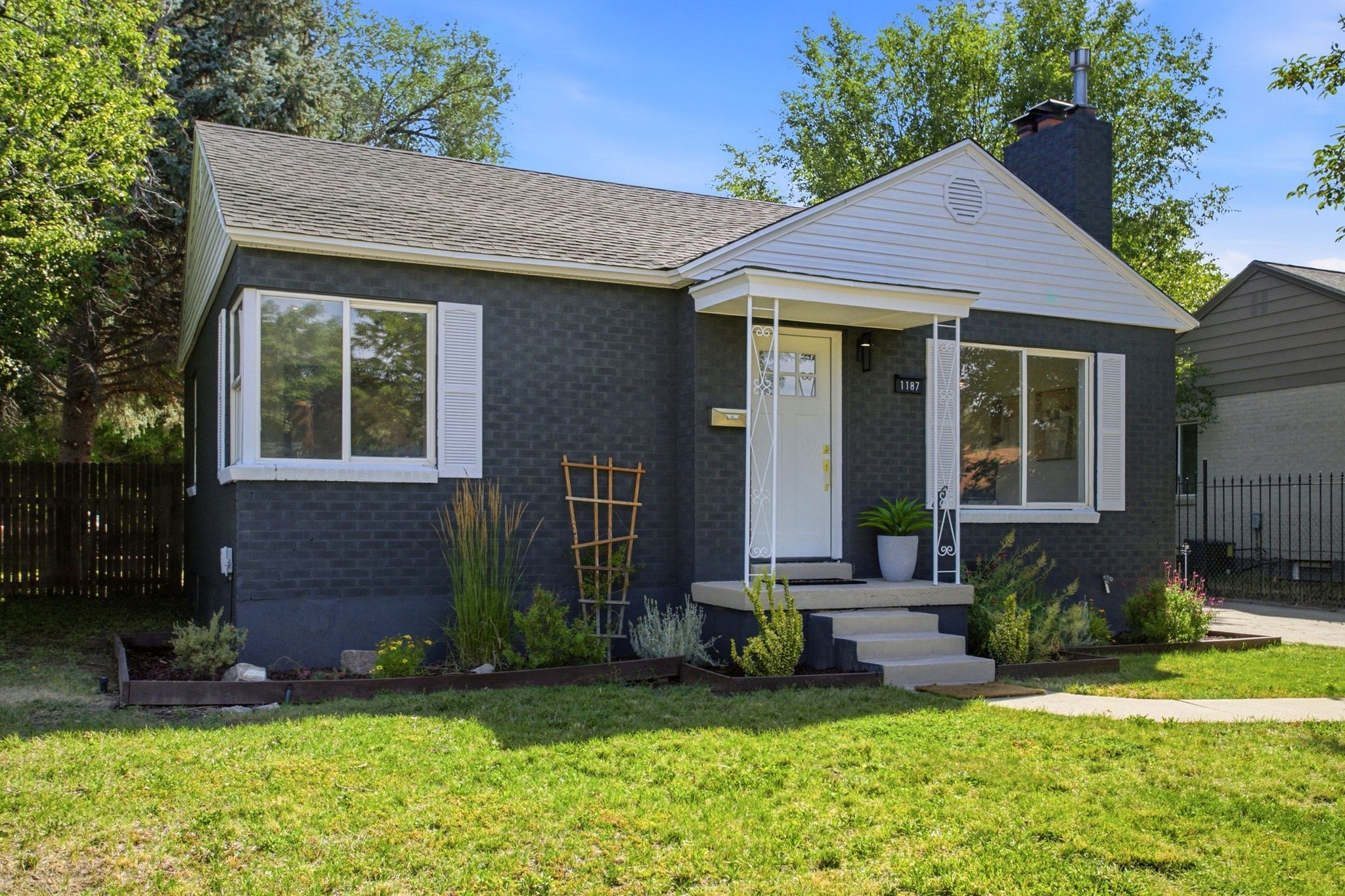 Charcoal-painted brick exterior with white trim, featuring a covered front porch, white front door, and a prominent chimney