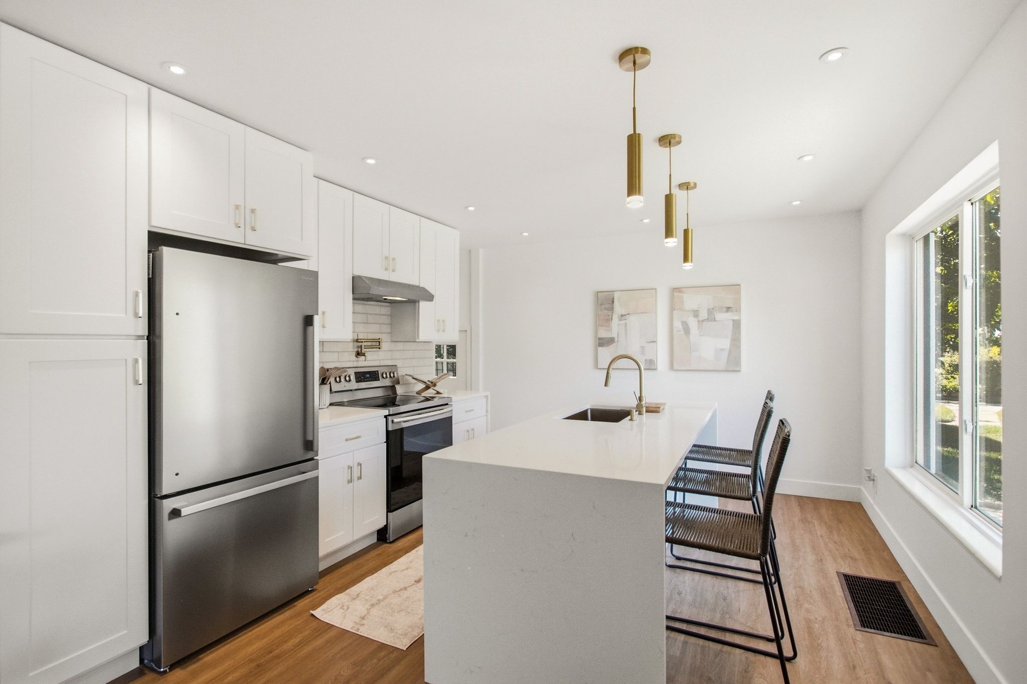 Contemporary kitchen featuring white shaker cabinetry, stainless steel appliances, a subway tile backsplash, and a large center island with integrated sink