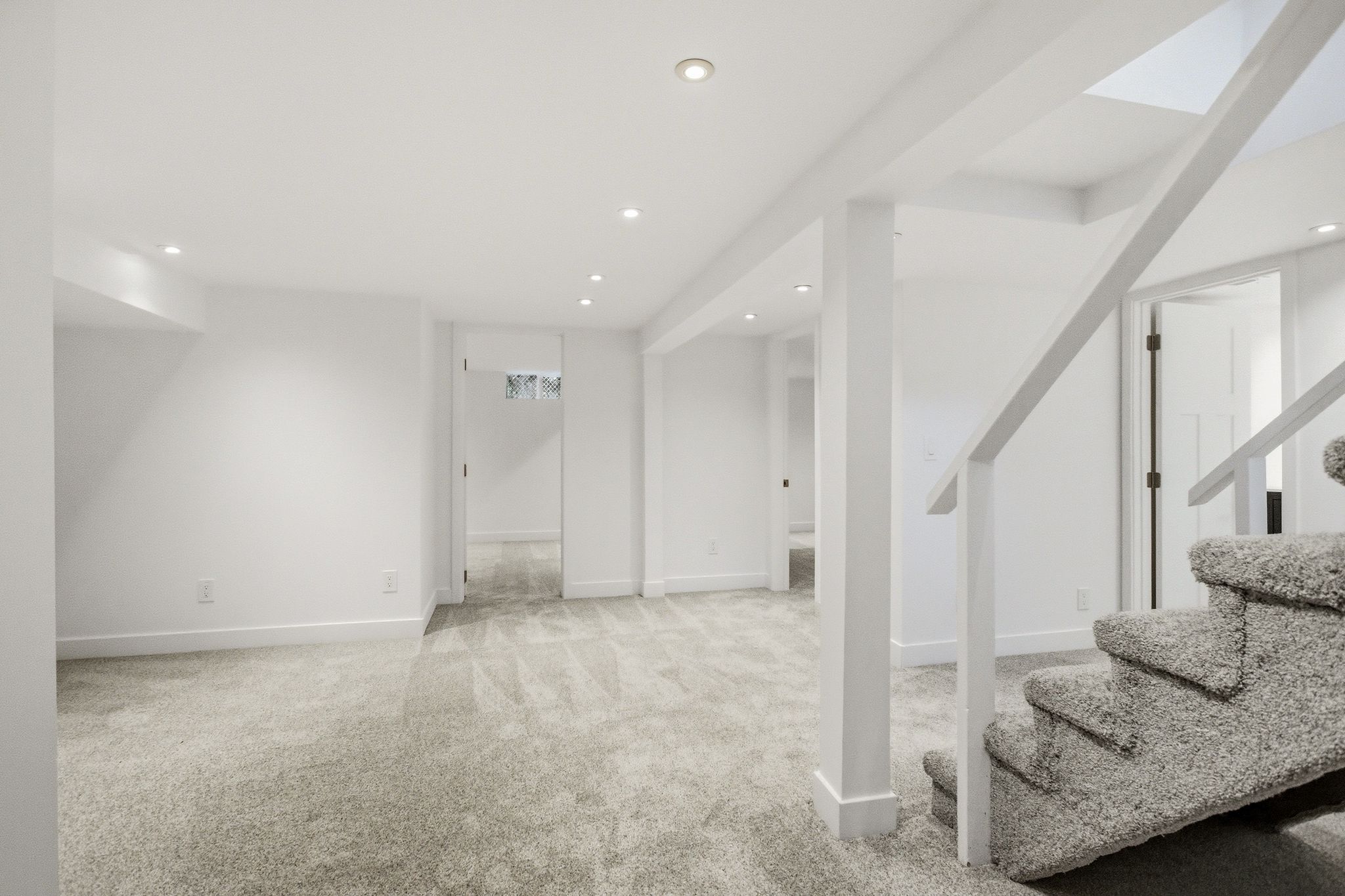 Carpeted lower level with recessed lighting, white walls, white trim, and white support columns