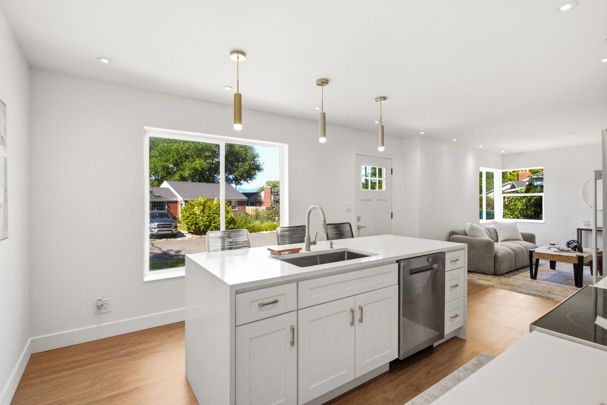 Open-concept kitchen featuring a large central island with integrated sink, stainless steel dishwasher, white cabinetry, and recessed lighting