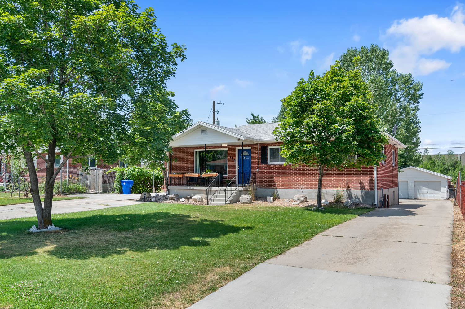 Brick residence featuring a covered front porch with railings, a multi-car driveway, mature trees, and a detached two-car garage