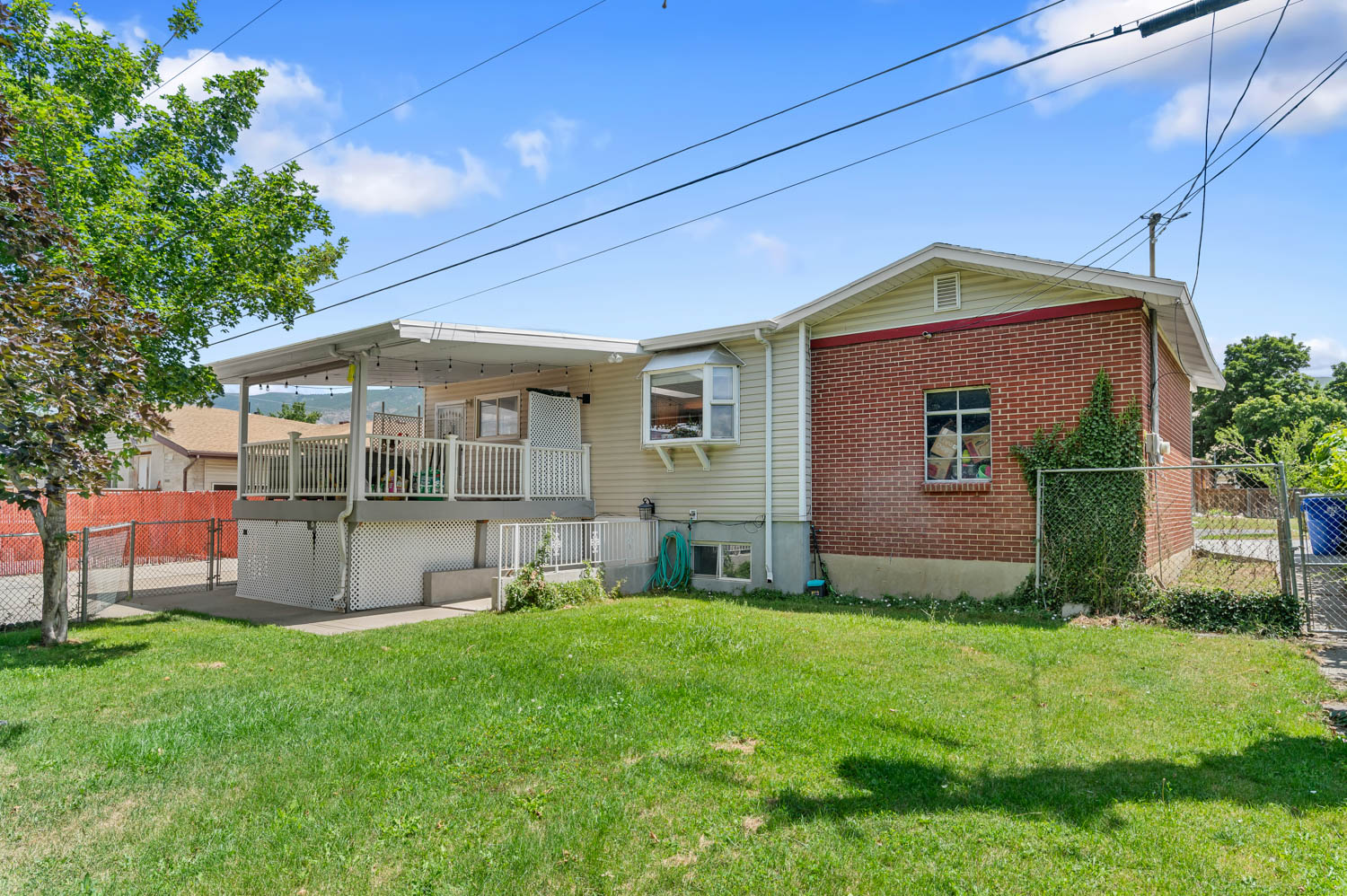 Expansive green lawn with a covered deck, white railing, and a chain-link fence