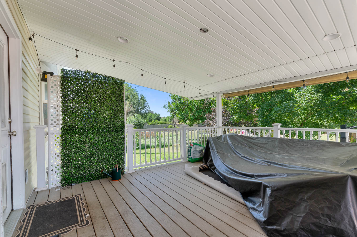 Covered outdoor deck with light wood-finish flooring, white railing, and a white beadboard ceiling featuring recessed lighting